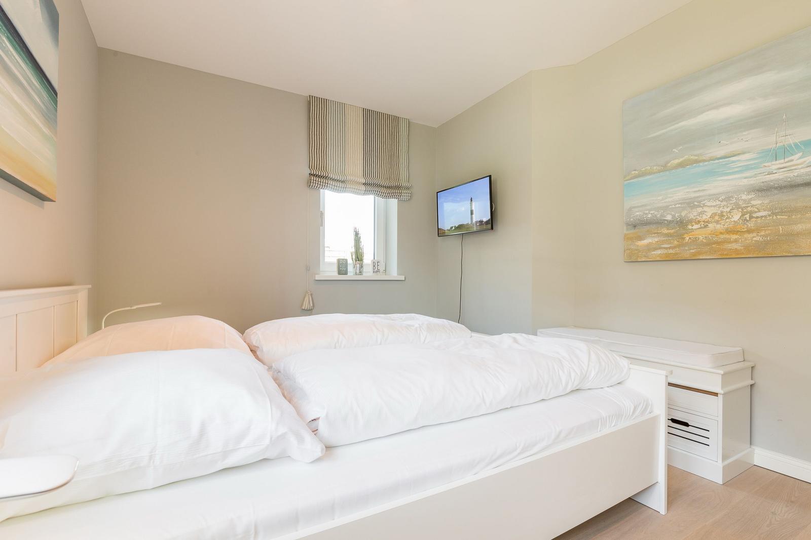 Schlafzimmer mit weißem Bett, Fenster, Wandbild und Fernseher.