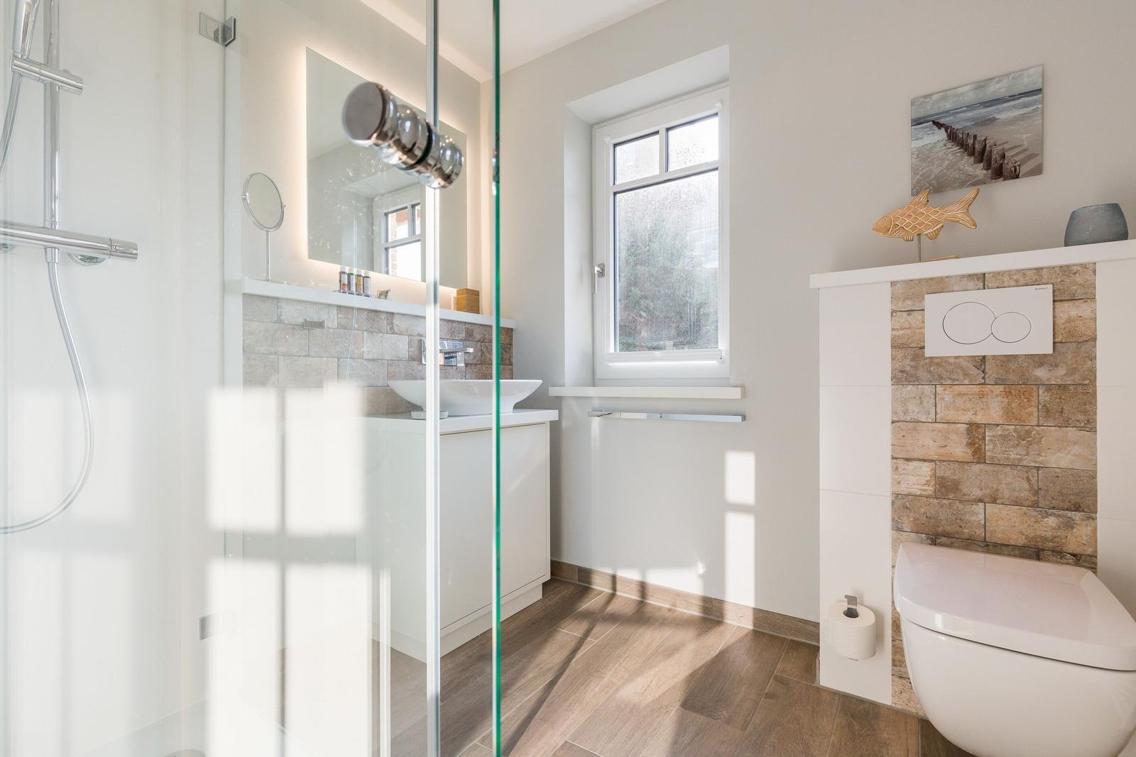 Badezimmer mit Dusche, Waschbecken und WC. Holzboden und Fenster.