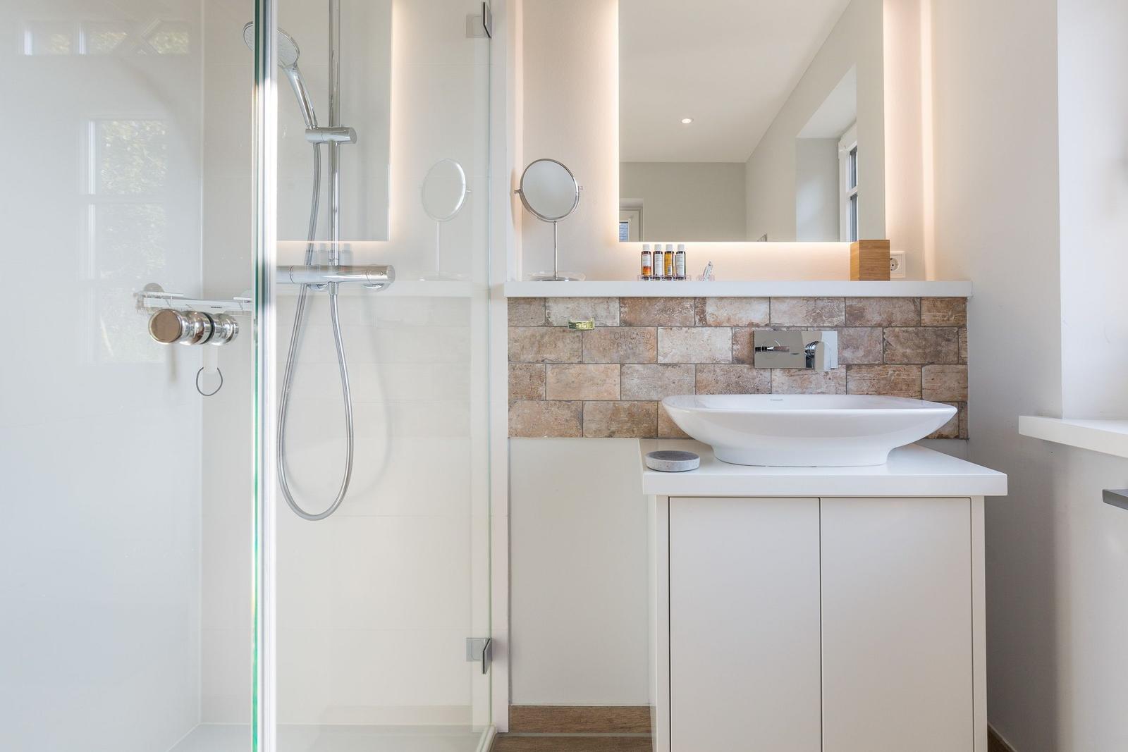 Bad mit Dusche, Waschbecken und beleuchtetem Spiegel.