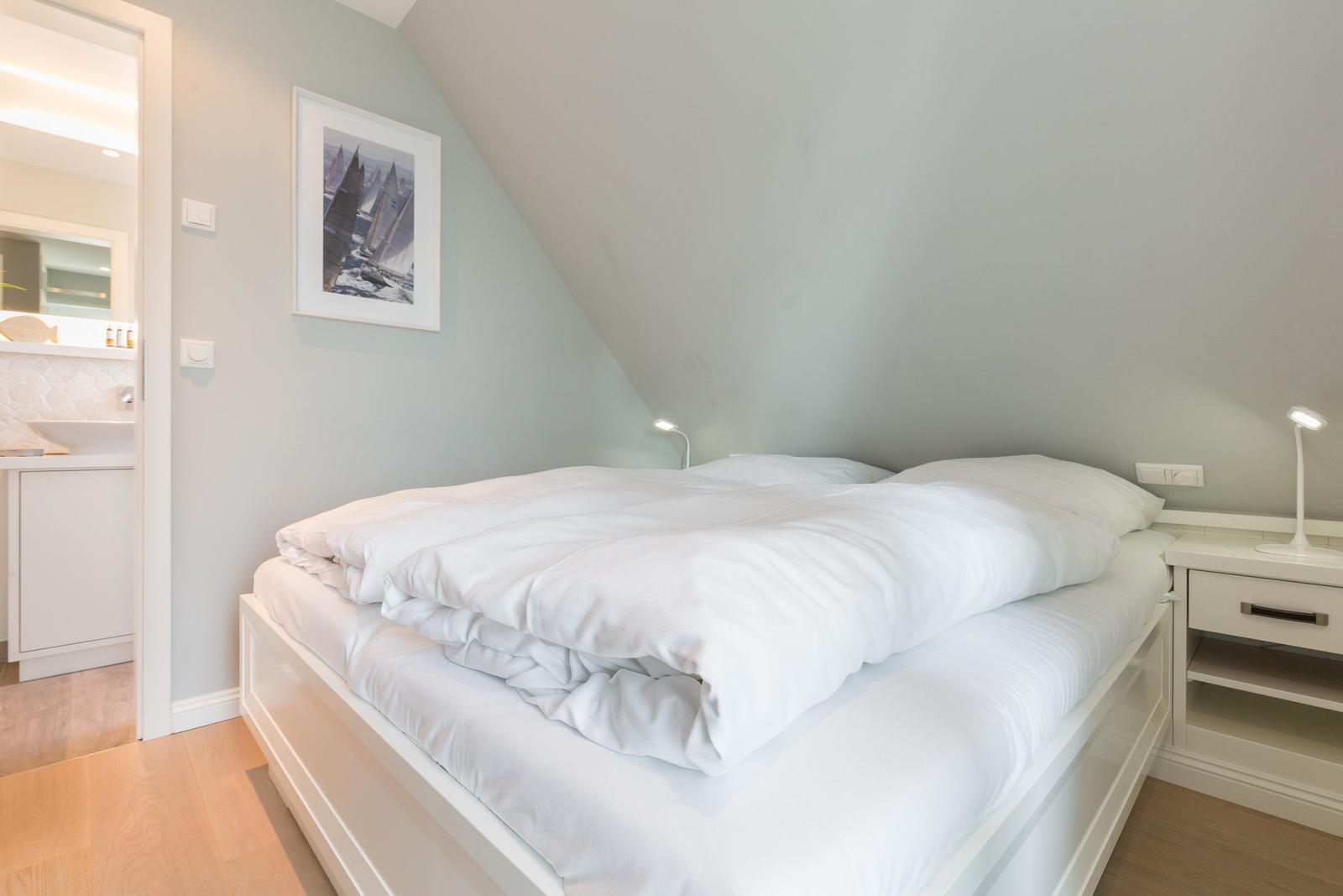 Schlafzimmer mit Doppelbett, Nachttisch und Bild an der Wand. Tür führt in die Badezimmer.