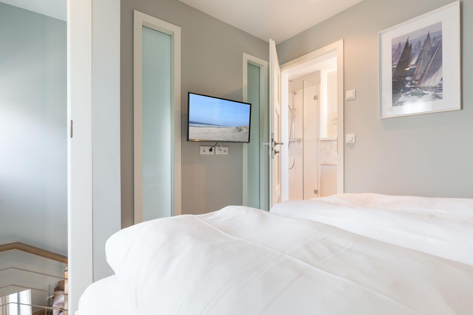 Schlafzimmer mit Bett, Fernseher und Blick in Bad