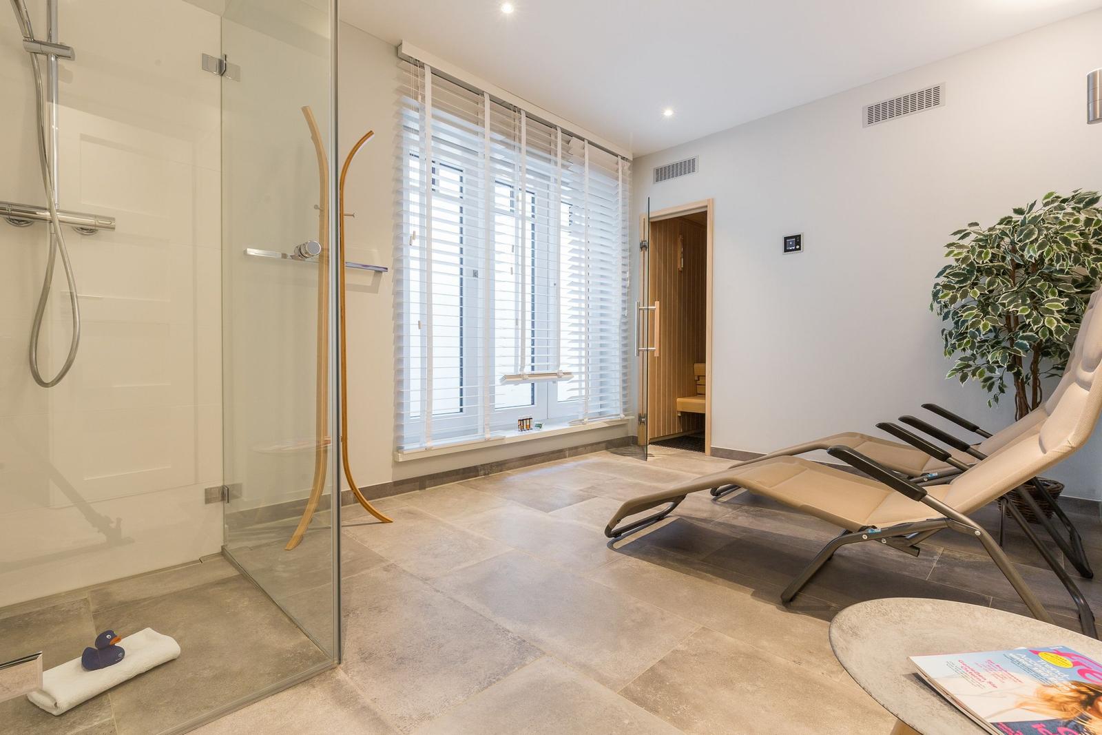 Dusche mit Glaswand, Liegestühle und Sauna im Hintergrund.