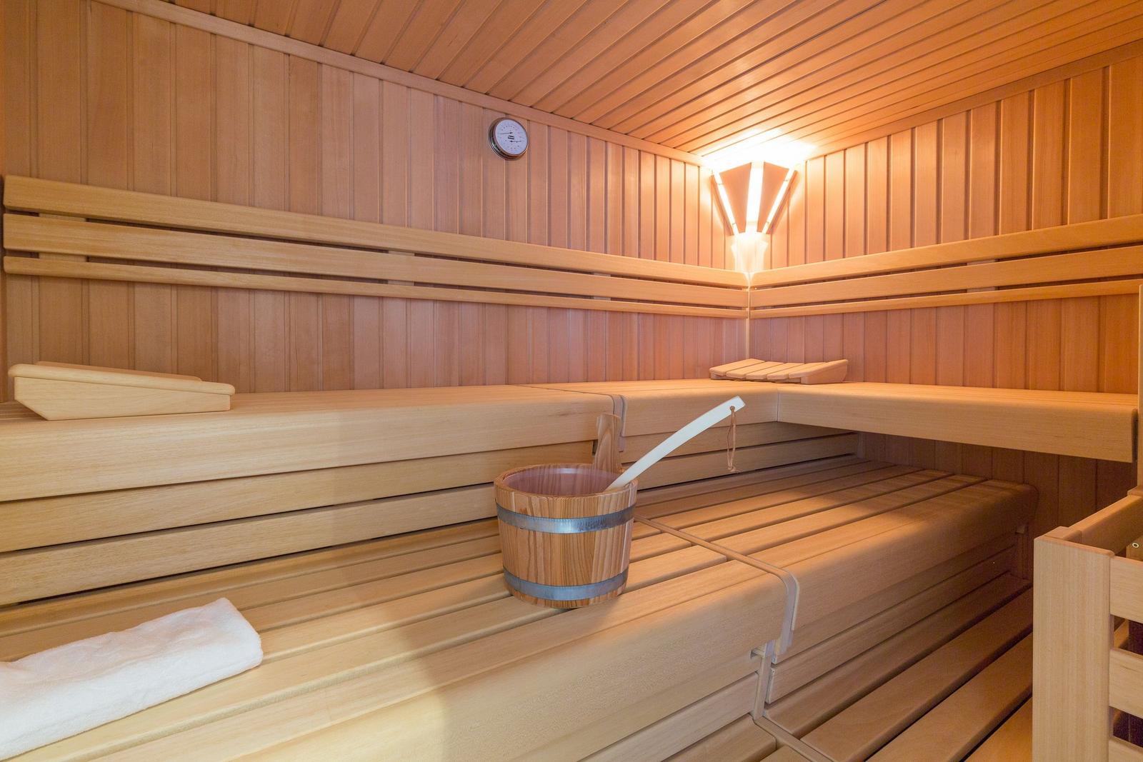 Sauna mit Holzbänken, Thermometer und Eimer mit Löffel.
