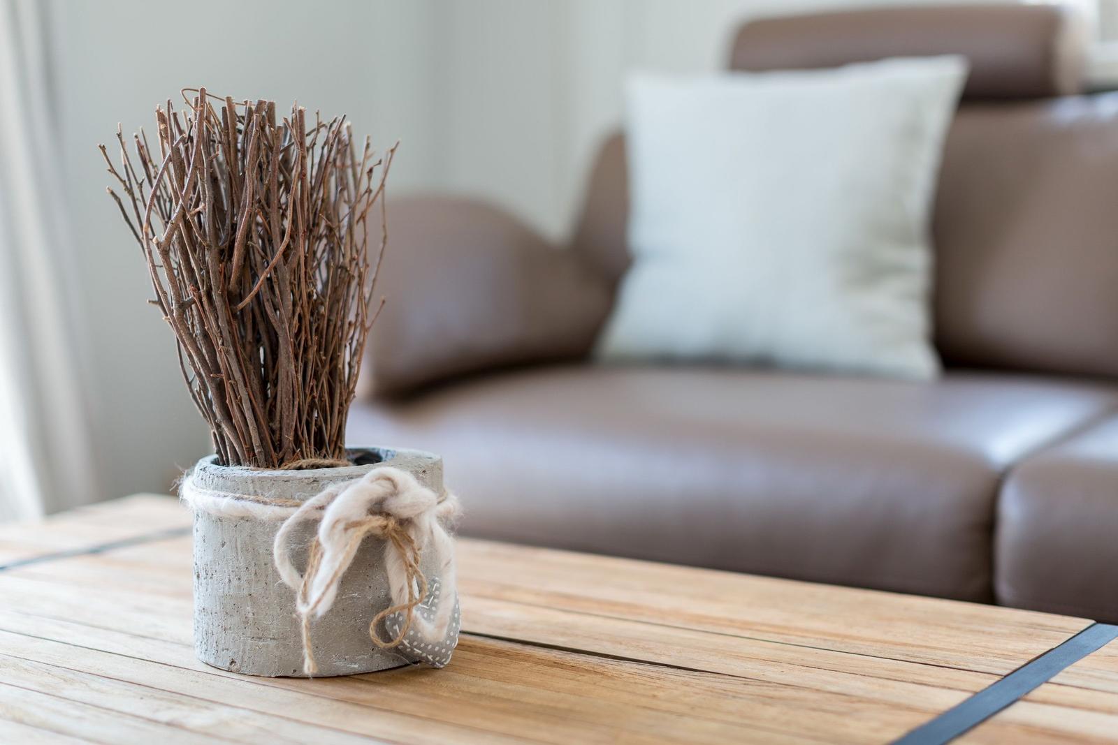 Holztisch mit Deko-Topf und Sofa im Hintergrund
