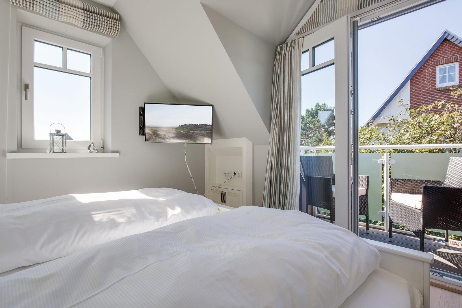 Bedroom with dormer window, TV, and balcony with seating.