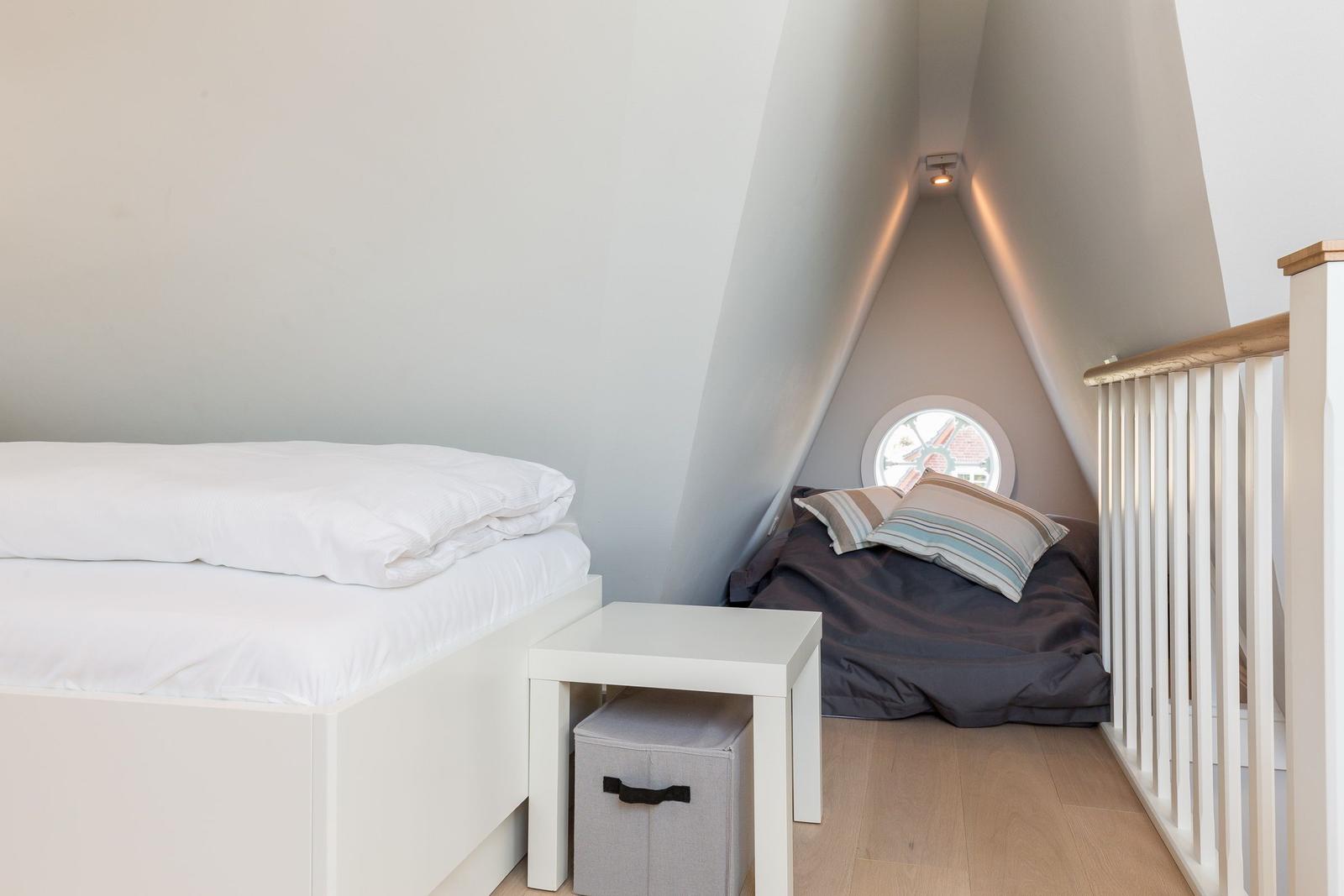 Room with sloped ceilings, white bed, and round window