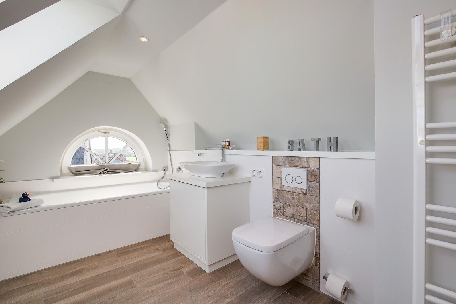 Bath with sink, toilet, and shower tub under sloped ceiling.