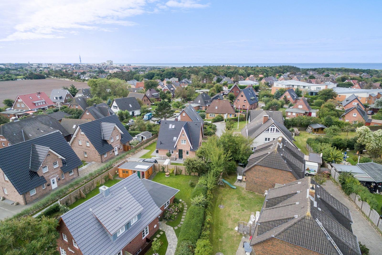 Aerial view of residential area with houses, gardens, and distant sea.