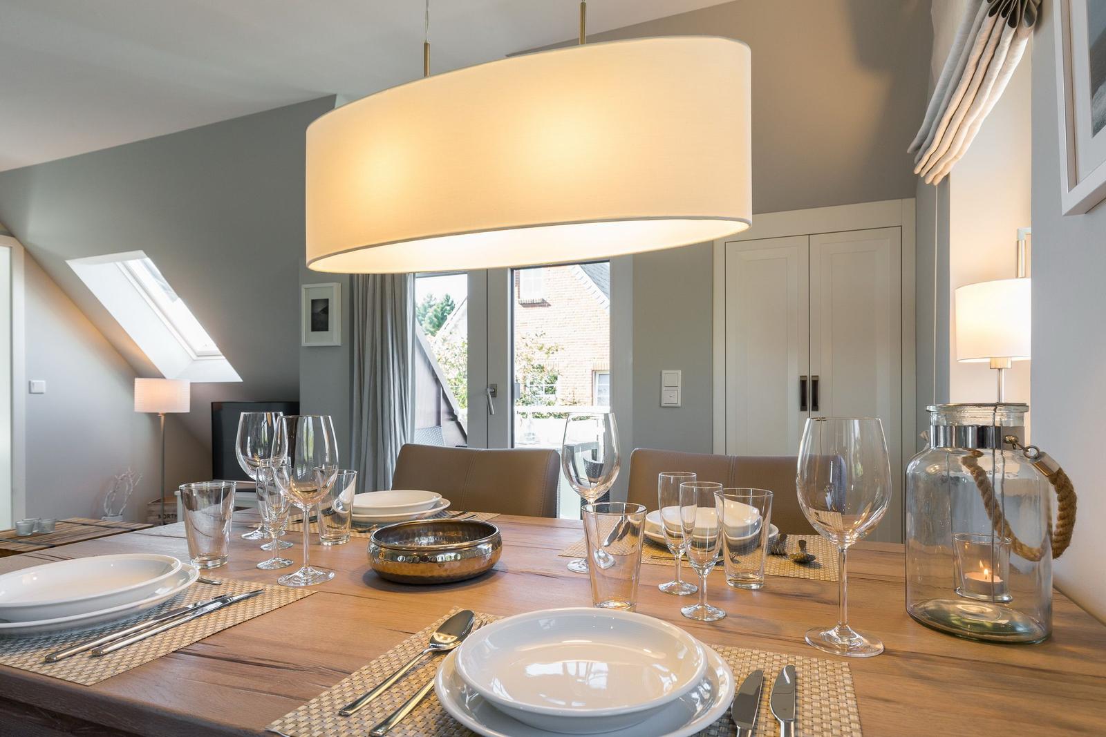 Dining room with wooden table, chairs, and pendant light. Windows and skylight provide daylight.