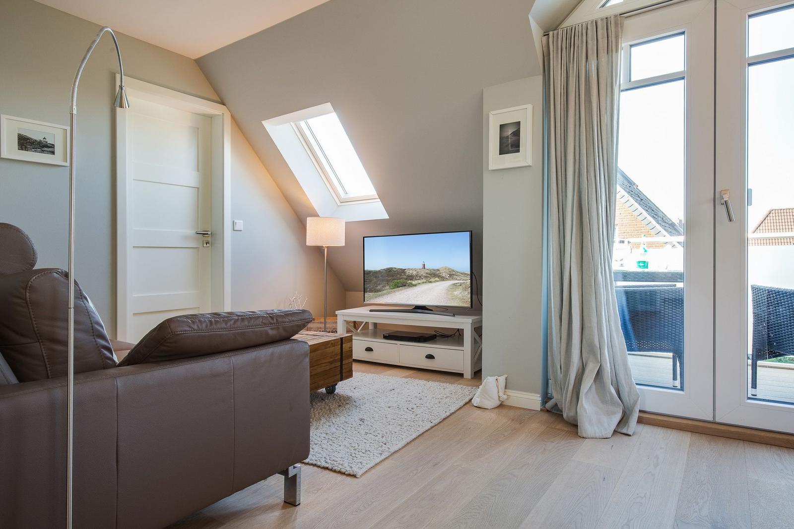 Living room with sofa, TV, and balcony door. Skylight and light wooden floor.