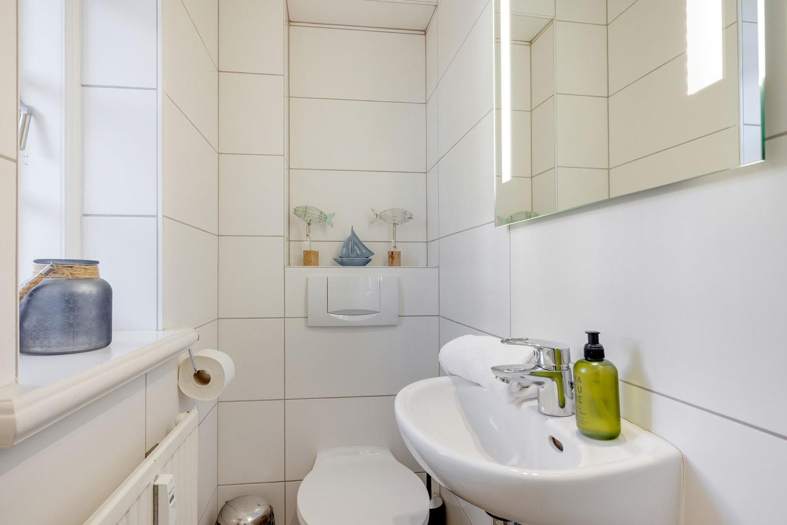 Badezimmer mit Waschbecken, Spiegel und Toilette. Dekorative Fische und Segelboot.