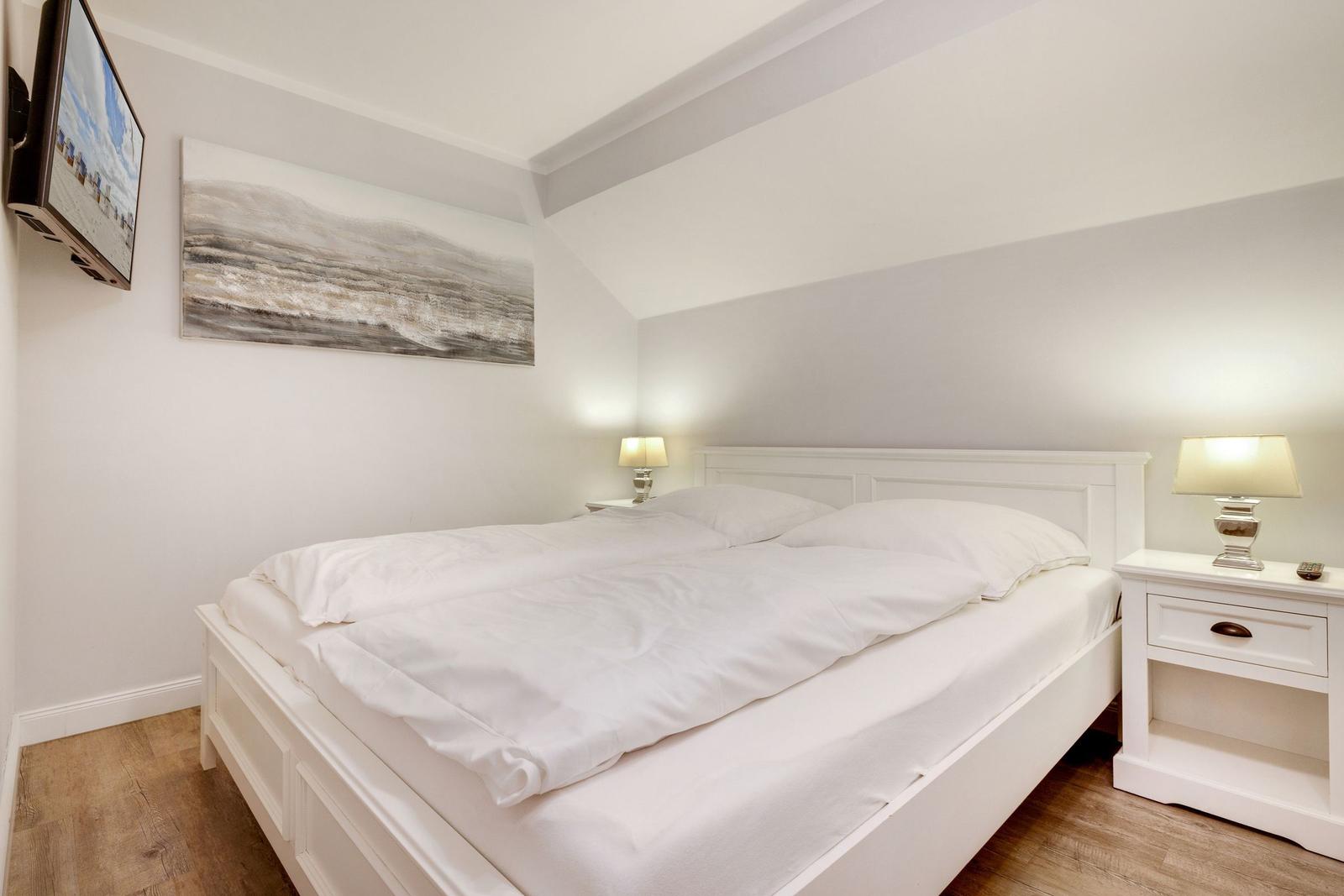 Schlafzimmer mit weißem Bett, Nachttischen und Wandbild.