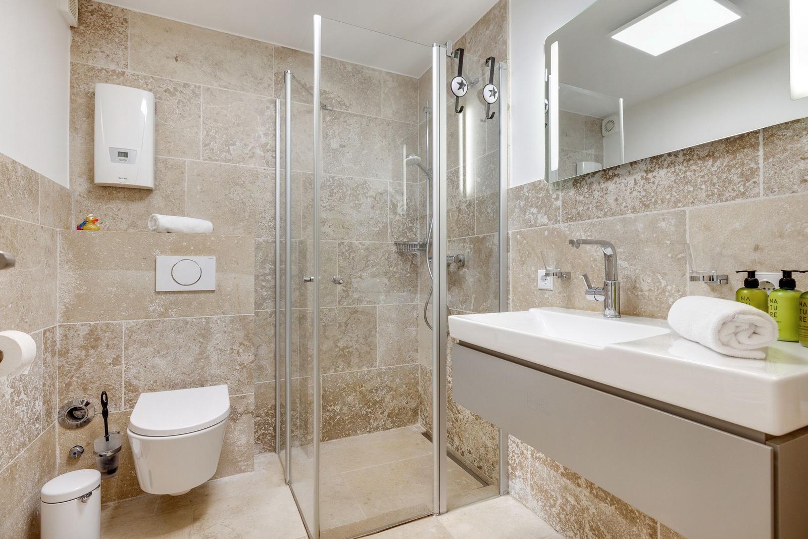 Badezimmer mit Dusche, Waschbecken und Toilette. Wandfliesen und Spiegel.