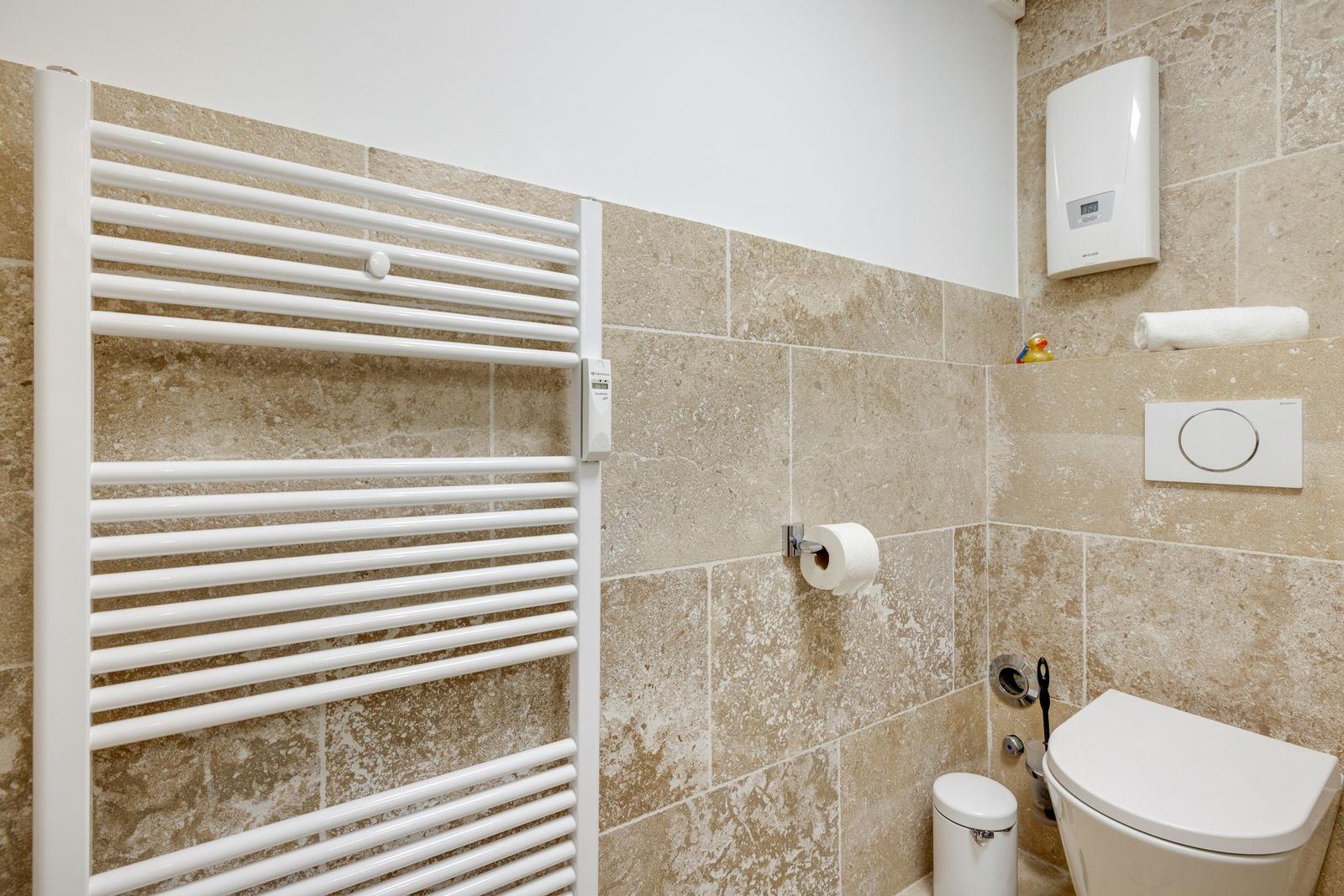 Badezimmer mit Heizkörper, Toilette und Toilettenpapierhalter an Steinwand.