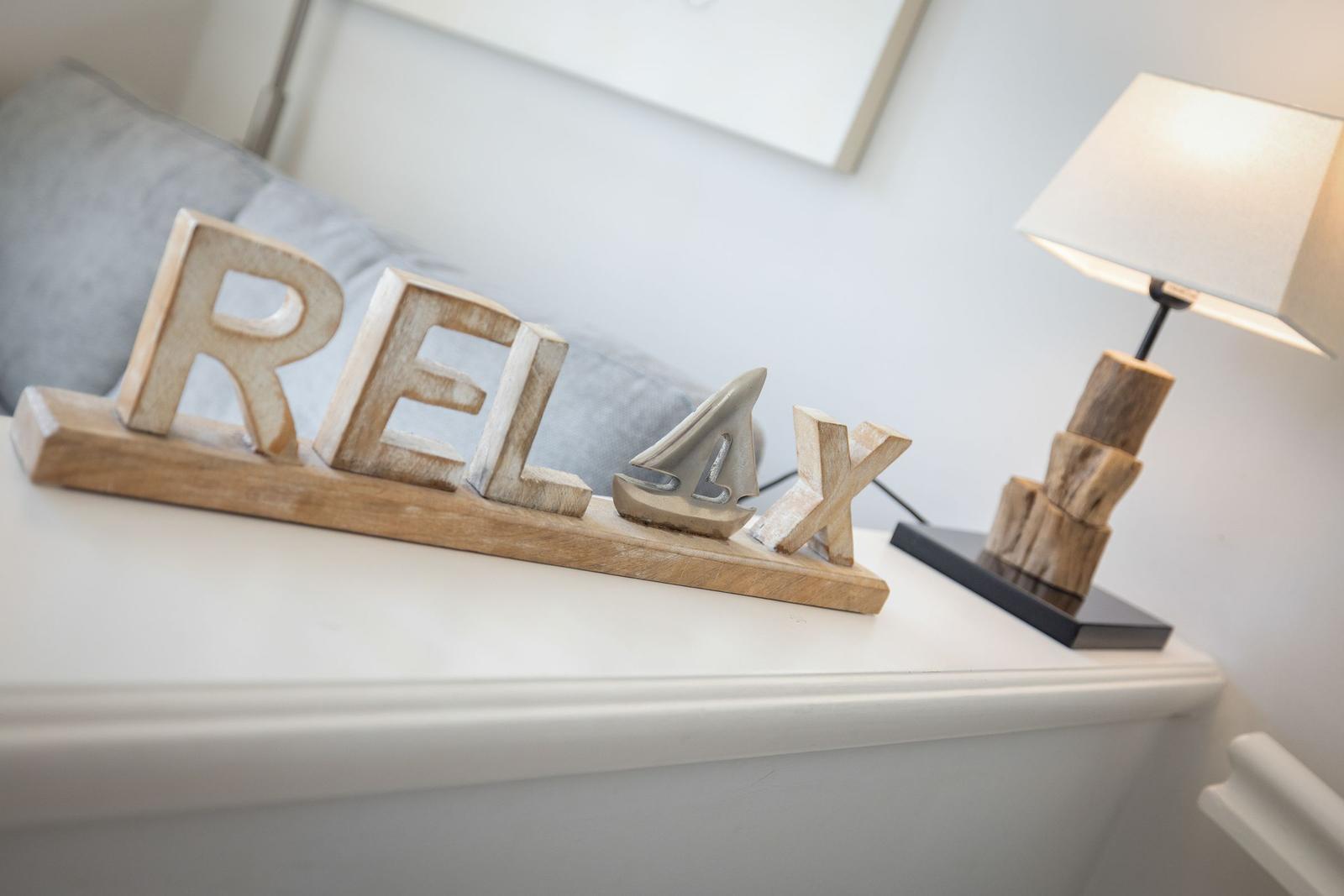 Auf dem Schreibtisch steht ein Holzschild mit der Aufschrift RELAX und eine Lampe.