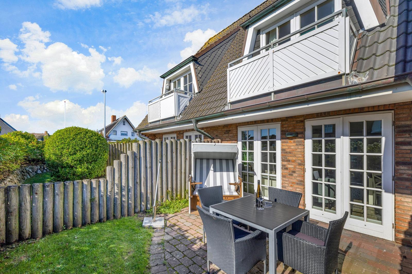Hinterhof mit Garten, Tisch, Stühlen und Strandkorb. Haus mit Balkon und Fenstern.