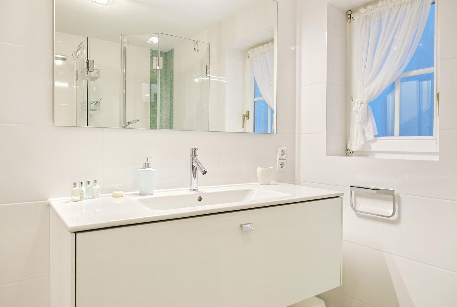 Badezimmer mit Waschbecken, Spiegel und Fenster mit Vorhang.