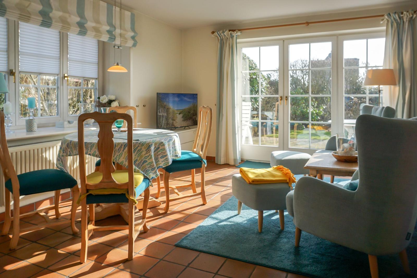 Essbereich mit Tisch und Stühlen, Sitzbereich mit Sofa und Teppich, Fenster mit Blick auf Garten.