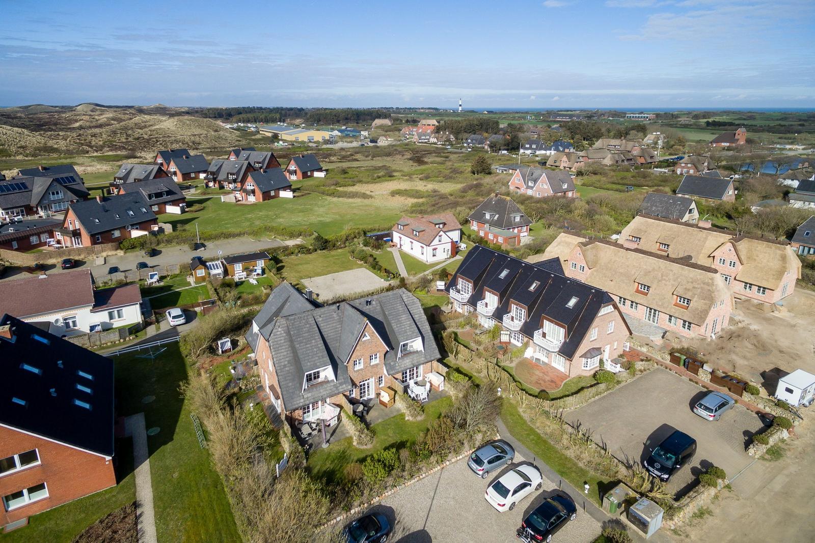Luftbild von Ferienhäusern mit Grünflächen und Blick auf die Dünen.