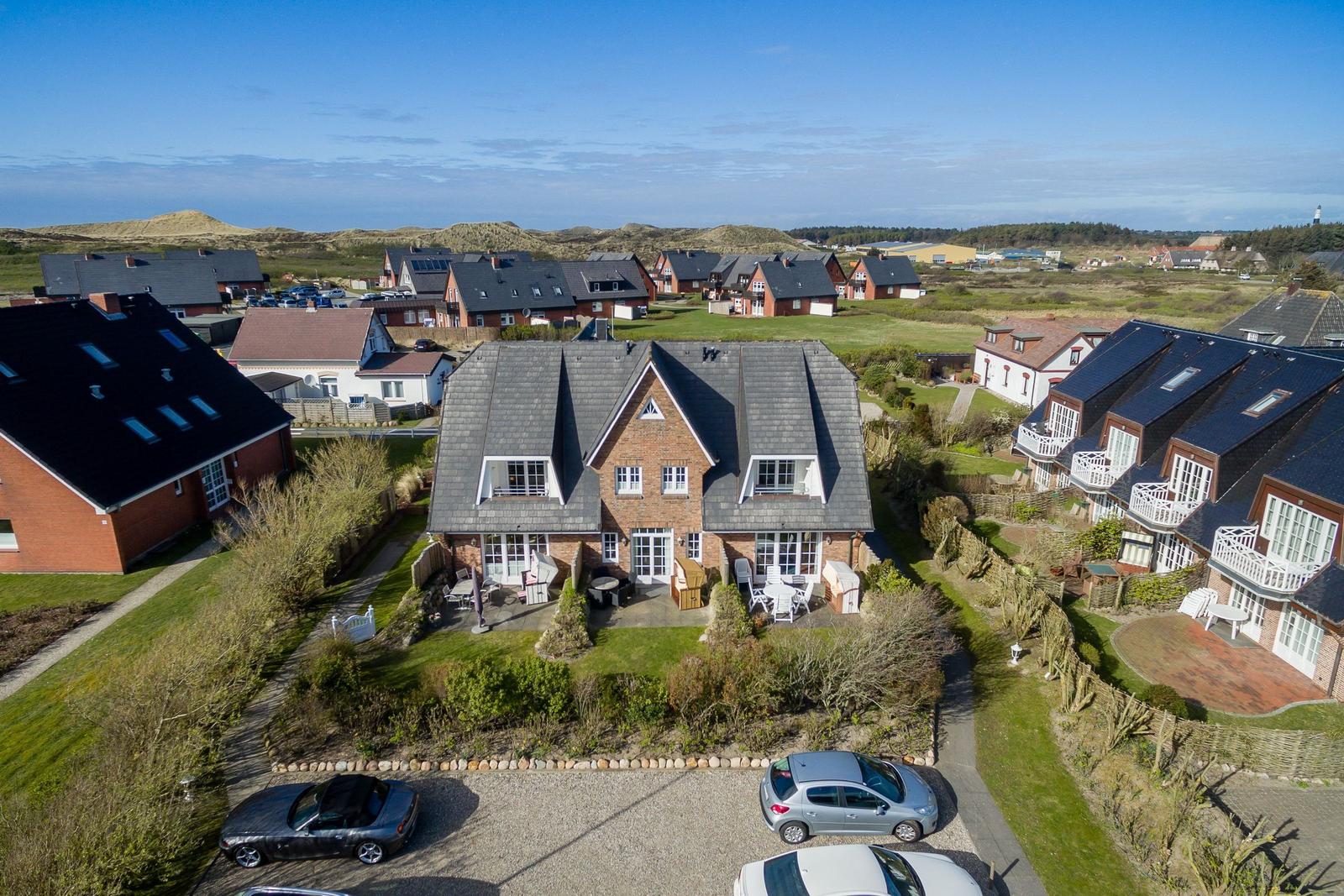 Haus mit Garten und Terrasse, umgeben von weiteren Häusern und Dünen.