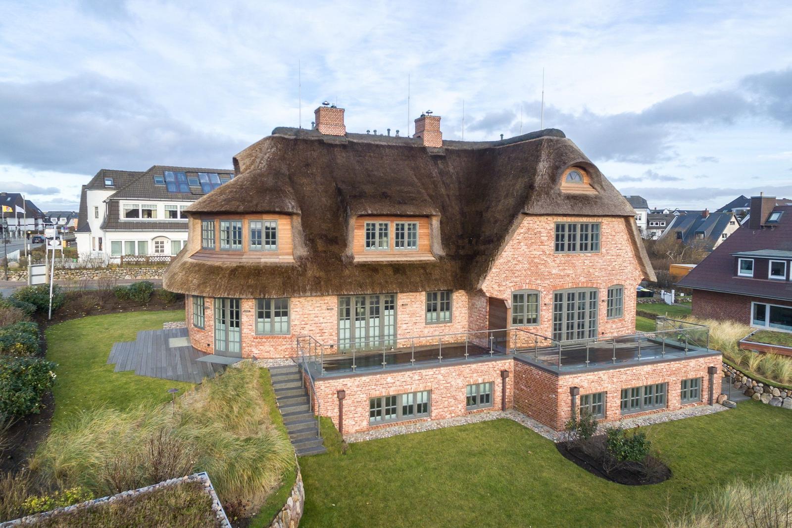 Haus mit strohgedecktem Dach und Backsteinfassade mit Terrasse und Garten.