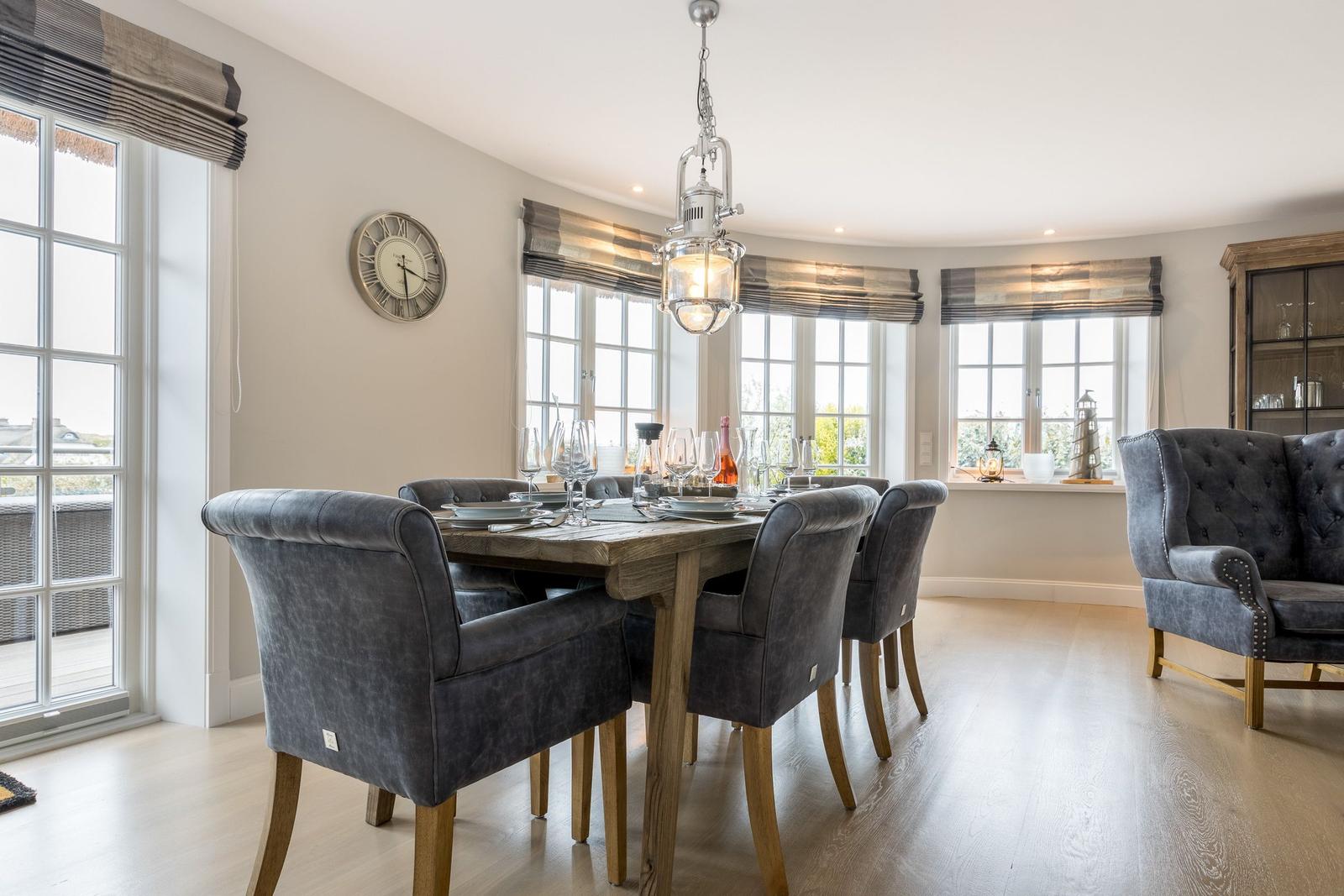 Esszimmer mit Holztisch, grauen Stühlen und großen Fenstern.