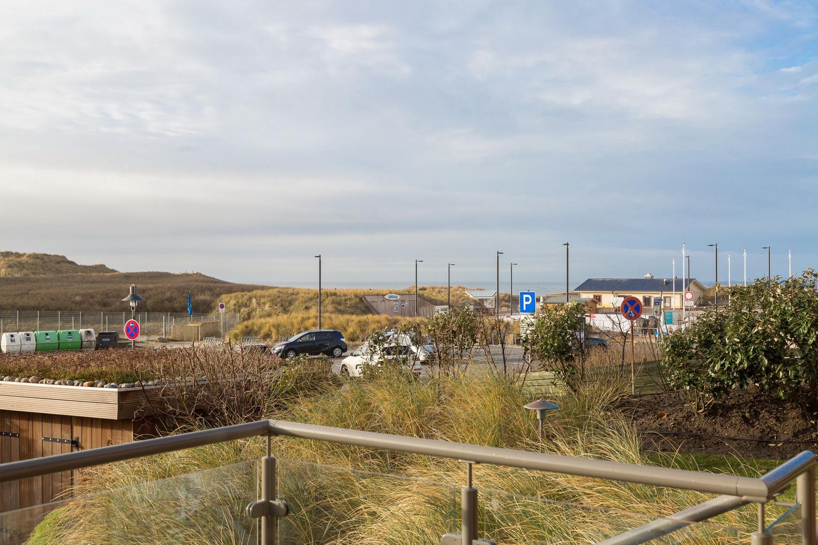 Blick auf Parkplatz, Dünen und Meer mit moderner Geländerbrüstung.