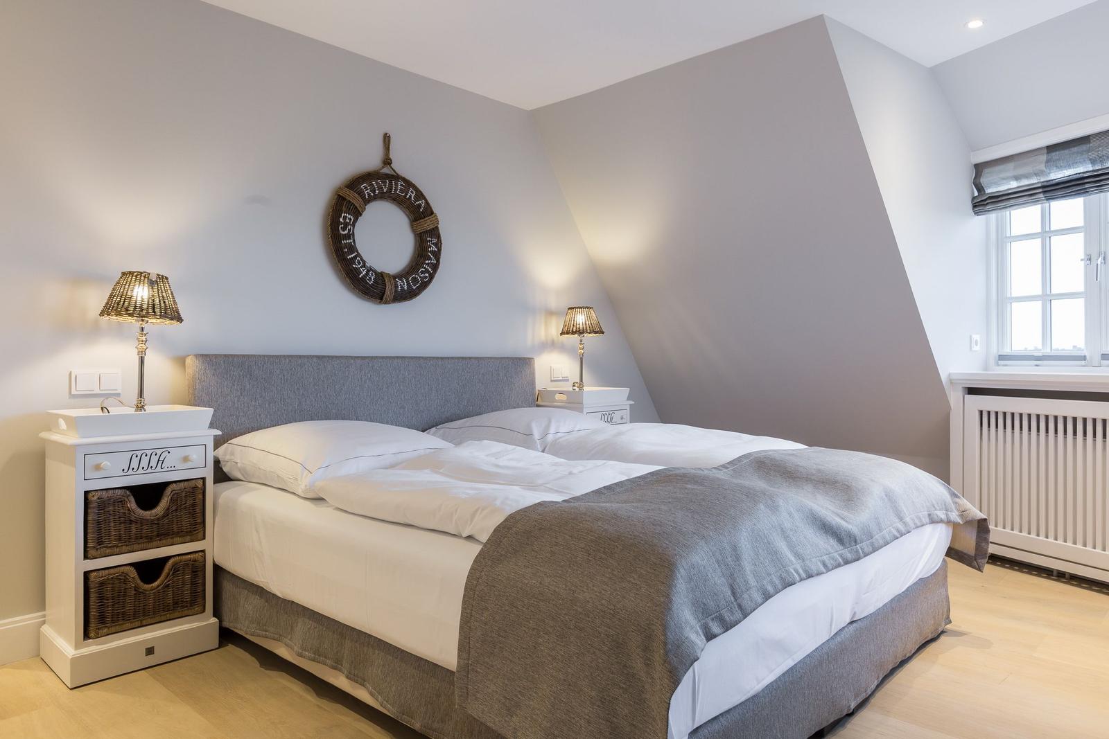 Schlafzimmer mit Doppelbett, zwei Nachttischen und Fenster. Wanddekoration mit Rettungsring.