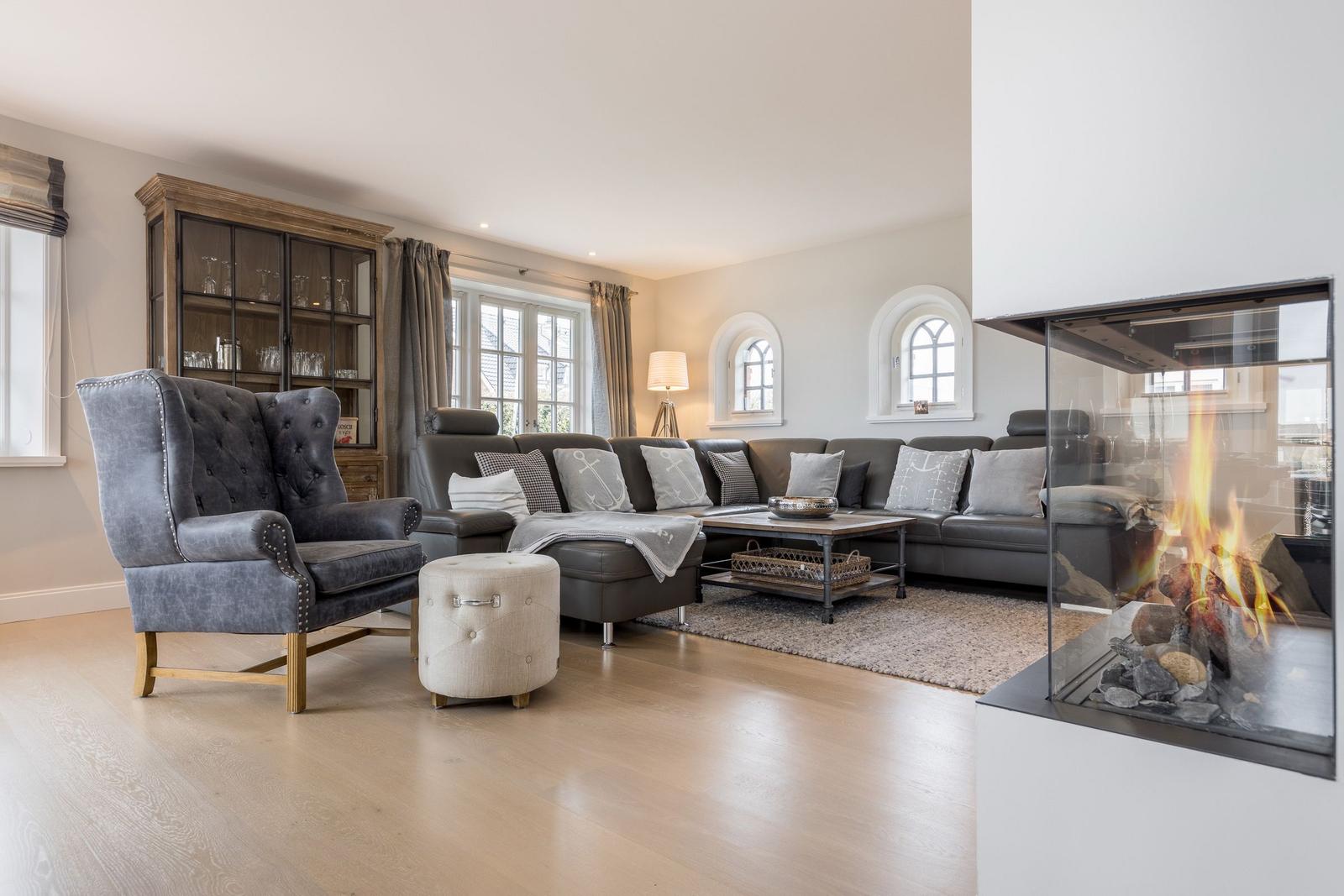 Wohnzimmer mit Sofa, Sessel und Kamin. Holzboden und Fenster.