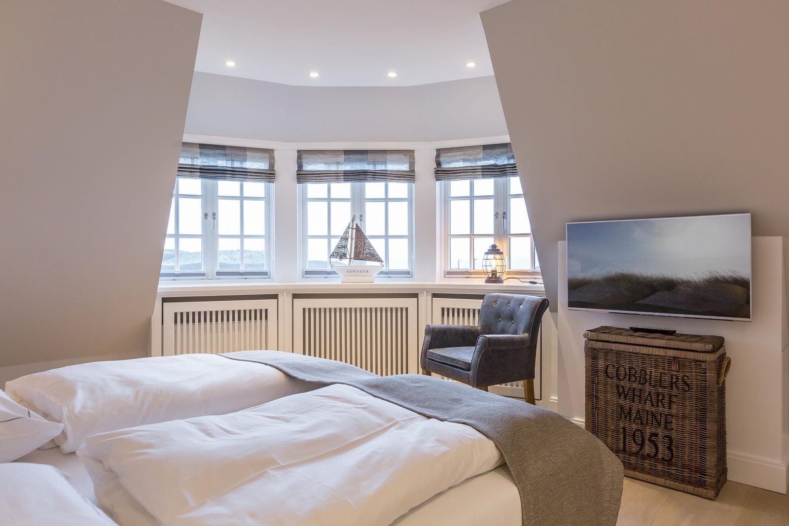 Schlafzimmer mit Blick aufs Meer, Bett, Sessel und Fernseher.