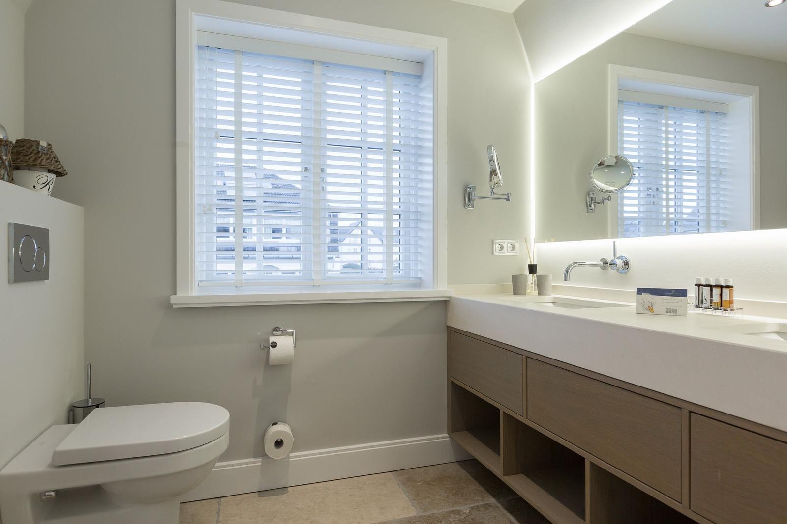 Badezimmer mit Toilette, Waschbecken und Fenster mit Jalousie.