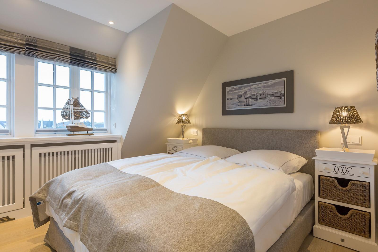 Schlafzimmer mit Doppelbett, Fenster und Nachttischen.