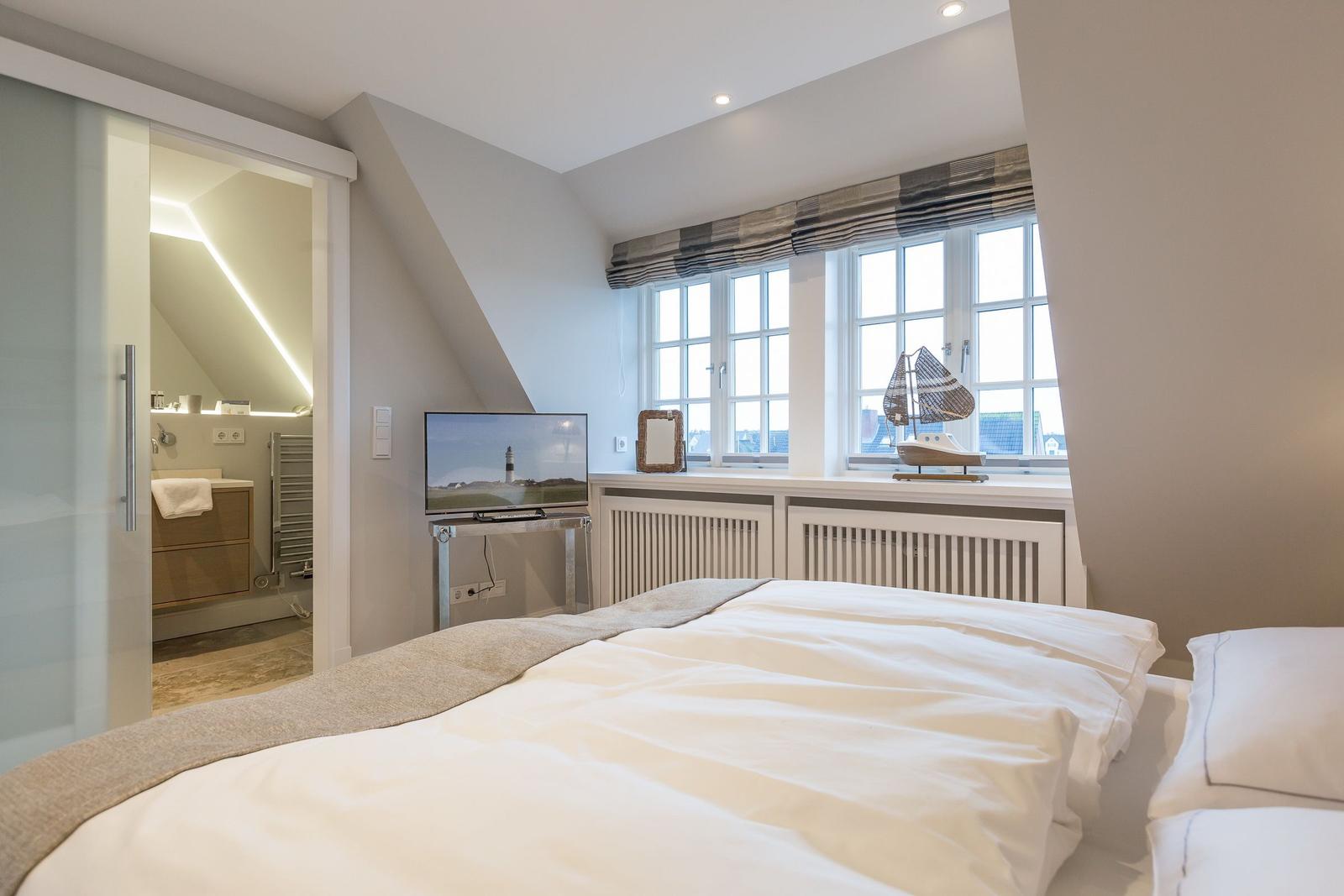 Schlafzimmer mit Dachschrägen, Fenster, TV und Blick in die Badewanne.