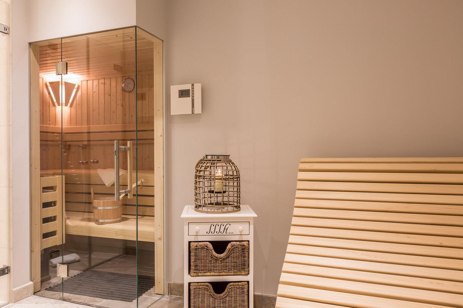 Sauna mit Glaswand, Holzbänken und kleinem Schrank mit Körben.