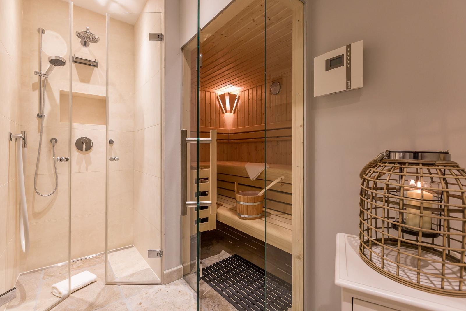 Dusche mit Regenduschkopf und Sauna mit Holzbänken und Holzwanne.