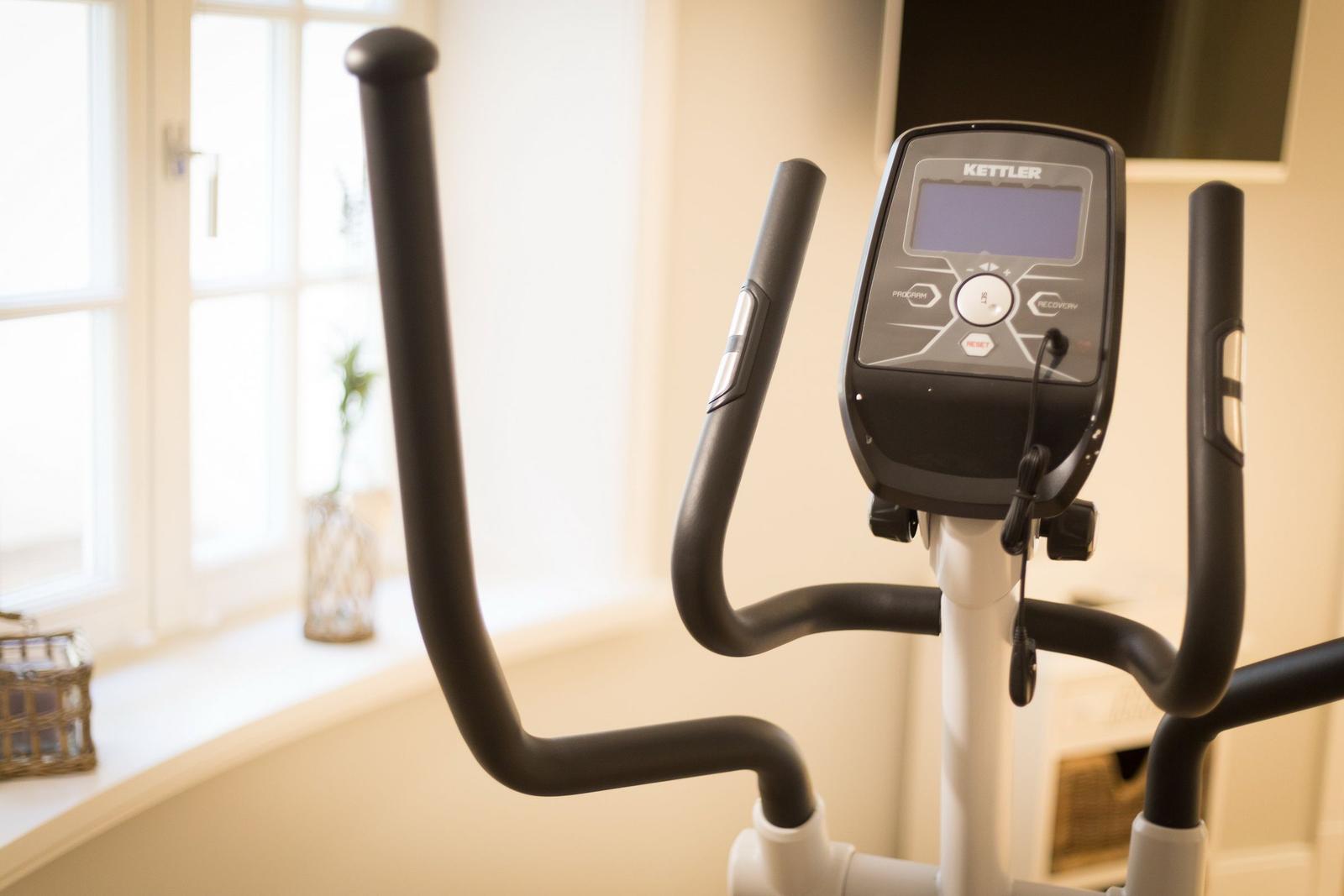 Elliptisches Fitnessgerät mit Display und Griffen in einem Raum mit Fenster.