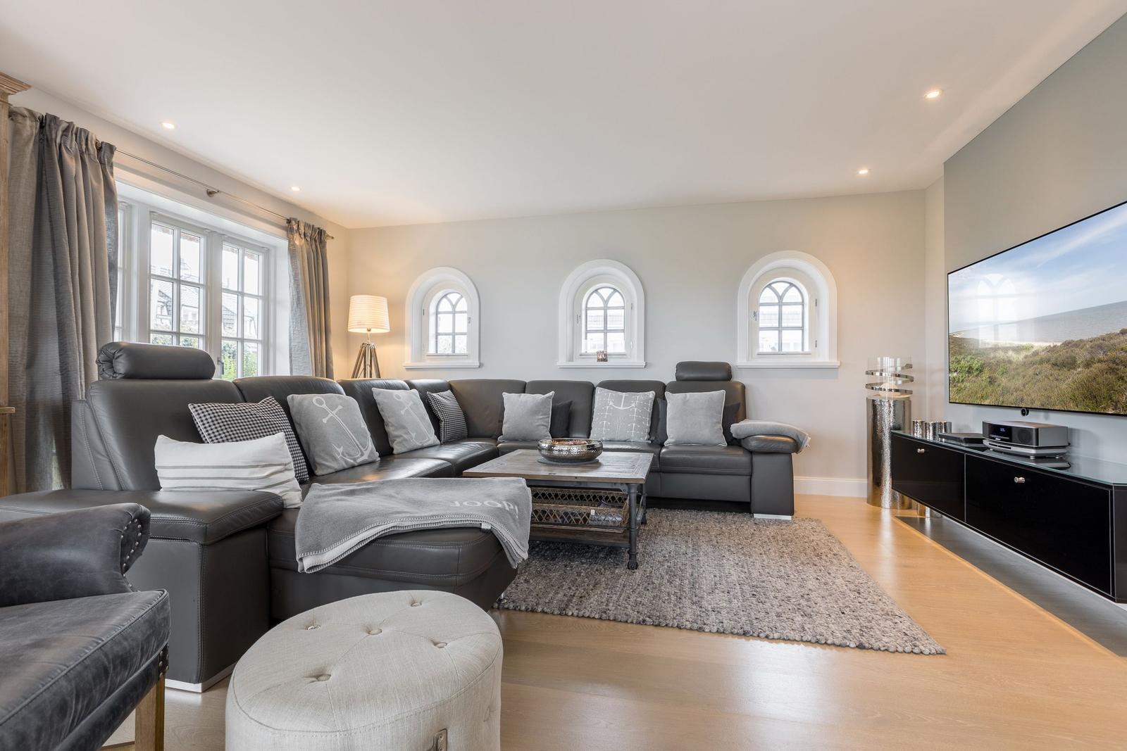 Wohnzimmer mit grauem Sofa, Holzboden und drei Bogenfenstern.