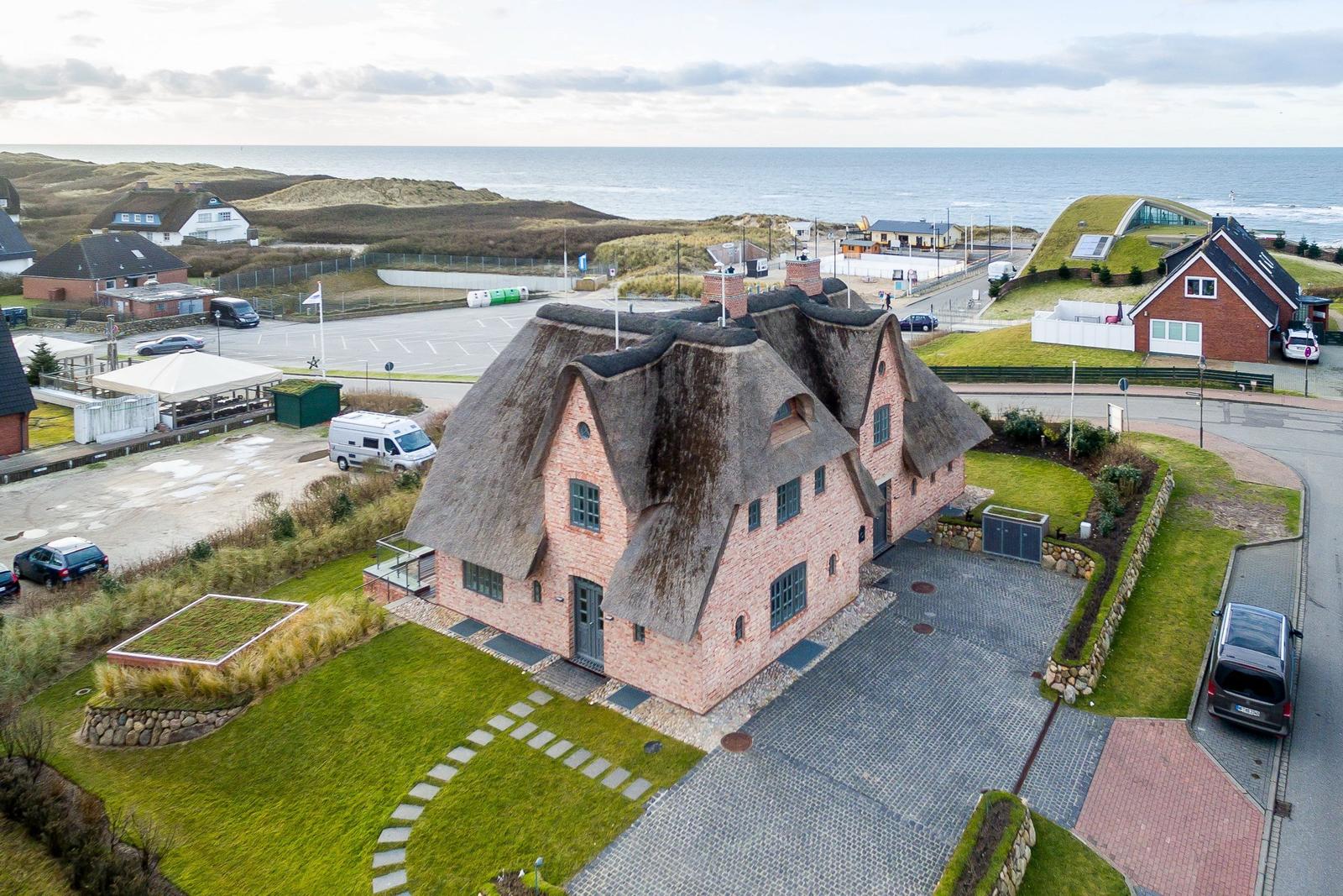 Haus mit Strohdach und Steinmauer, umgeben von Grünflächen und Meer.