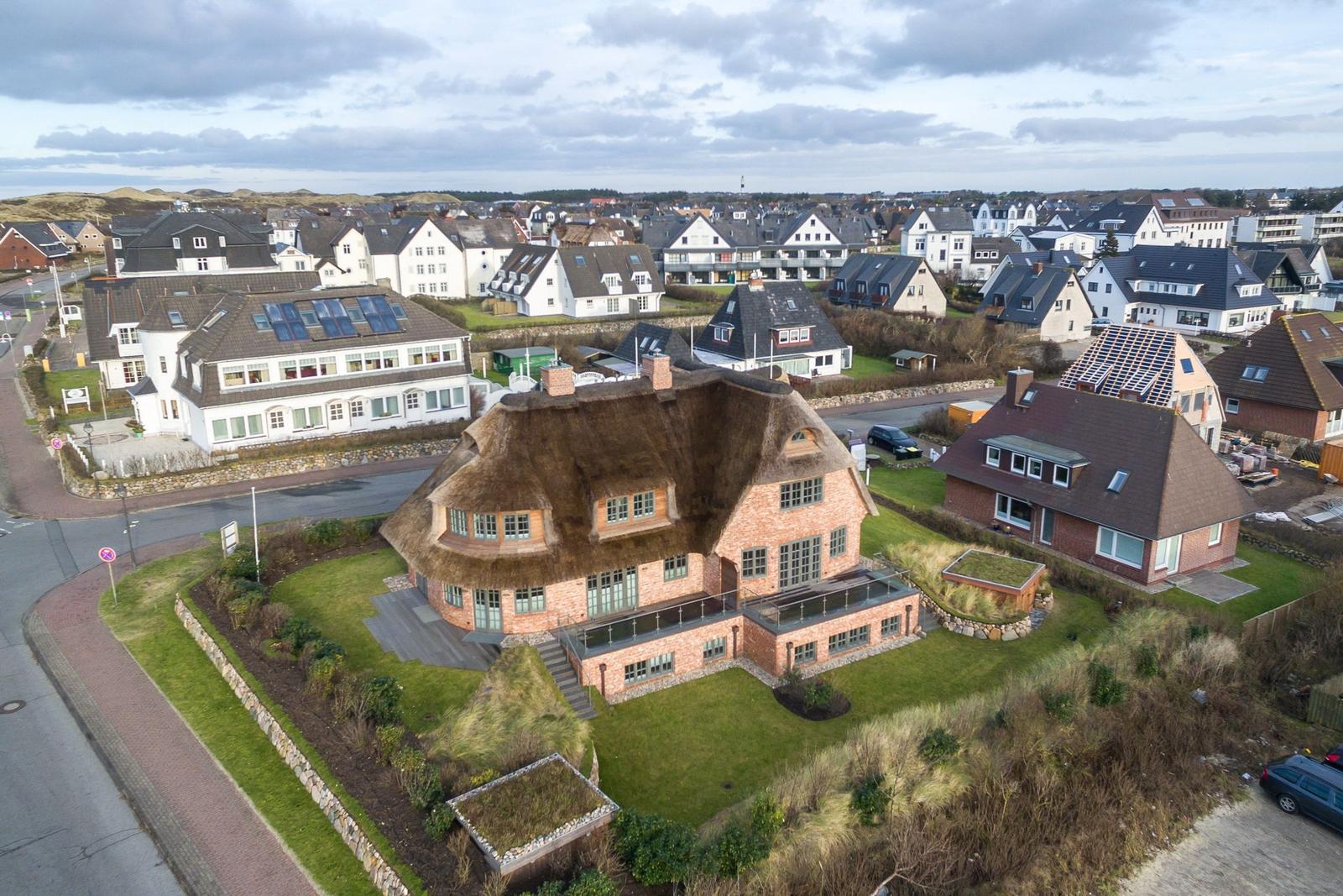 Dorfhaus mit Strohdach und Garten. Blick auf Wohngebiet mit Häusern und Straßen.