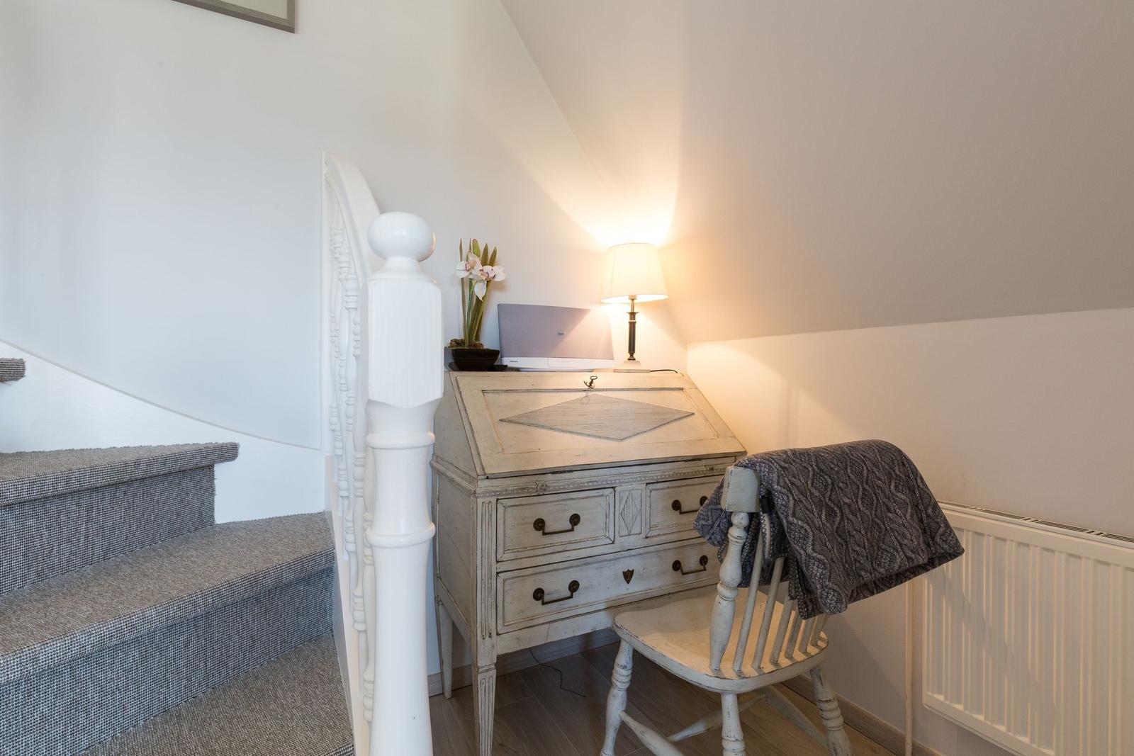 Desk with chair under sloped ceiling, next to staircase with white balustrade.