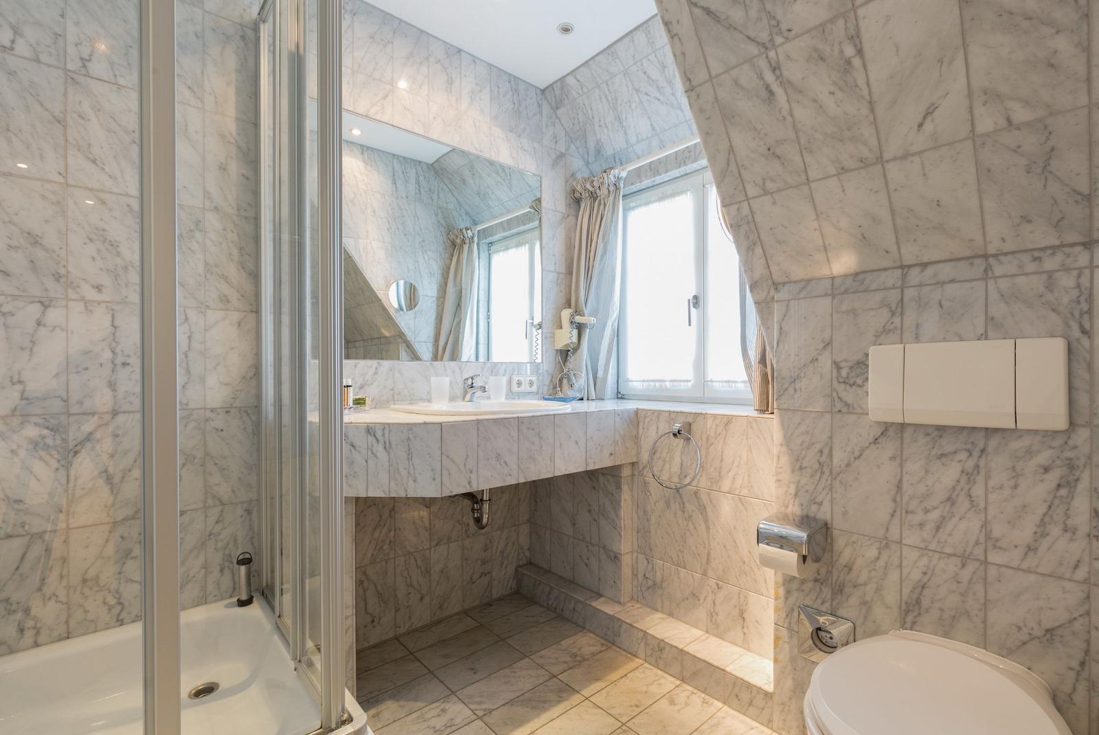 Bathroom with marble walls, shower, sink, and toilet.