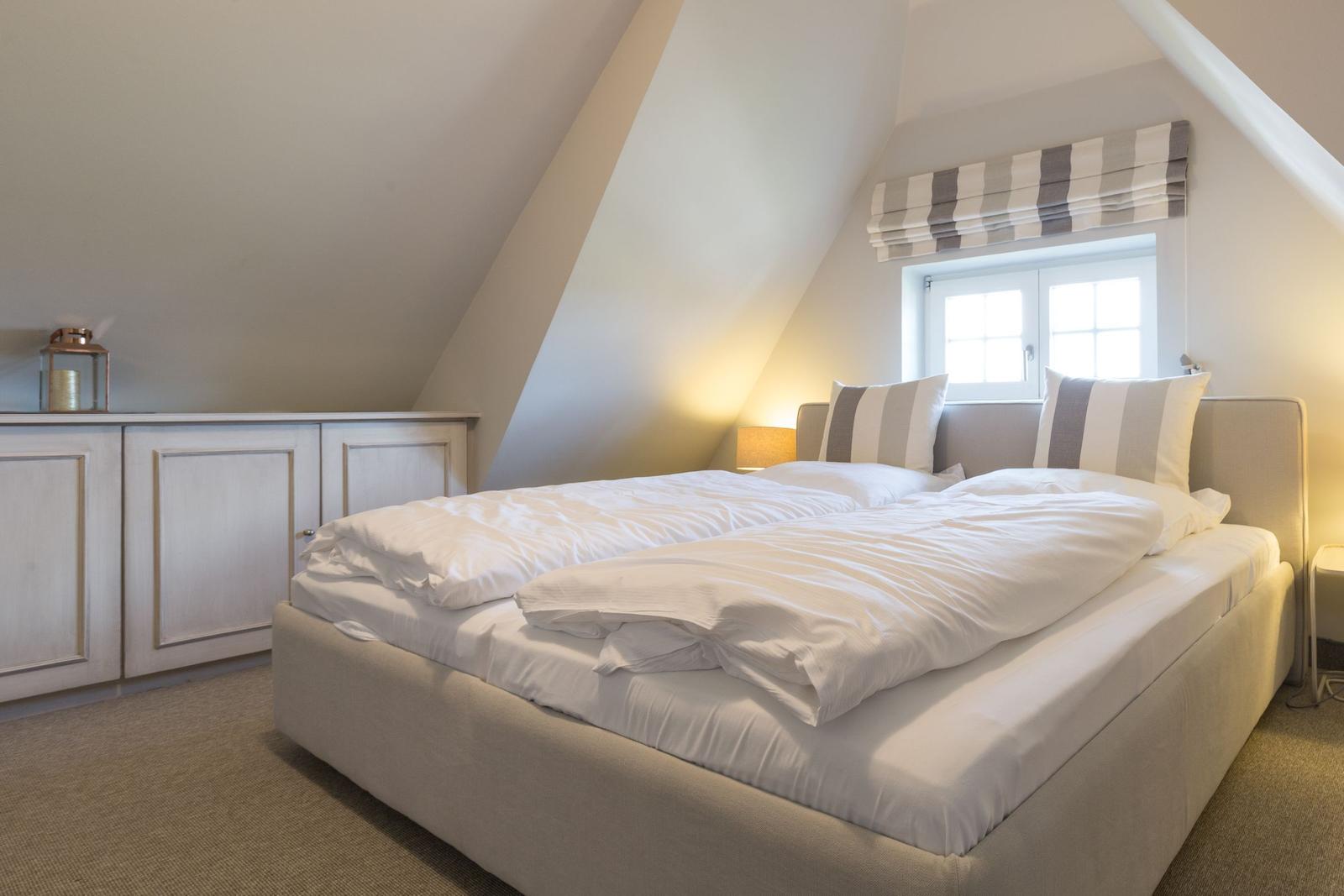 Bedroom with sloped ceiling, bed, and window with roller blind.