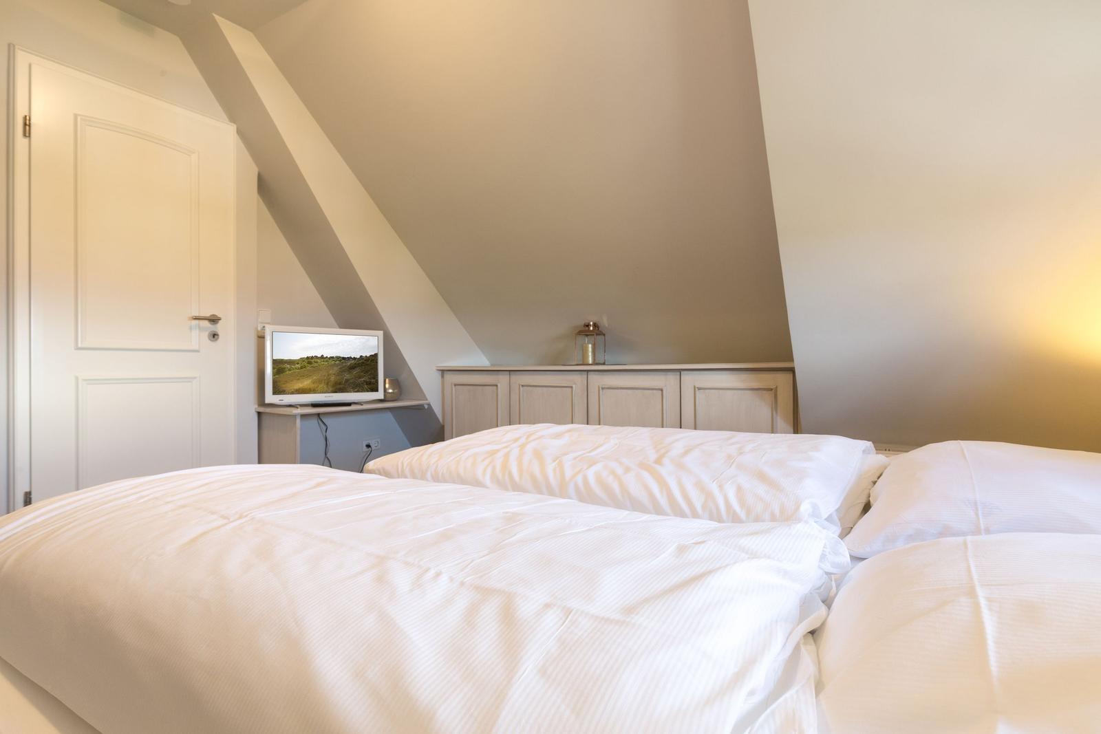 Bedroom with double bed, wardrobe, and TV under sloped ceiling.