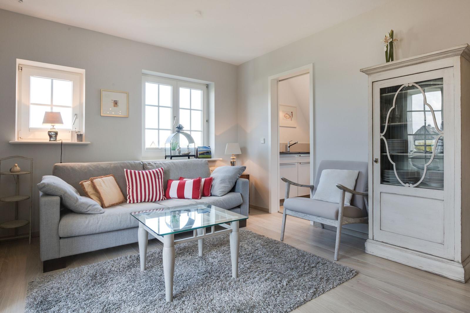 Living room with sofa, glass table, and cabinet. Passage to the kitchen.