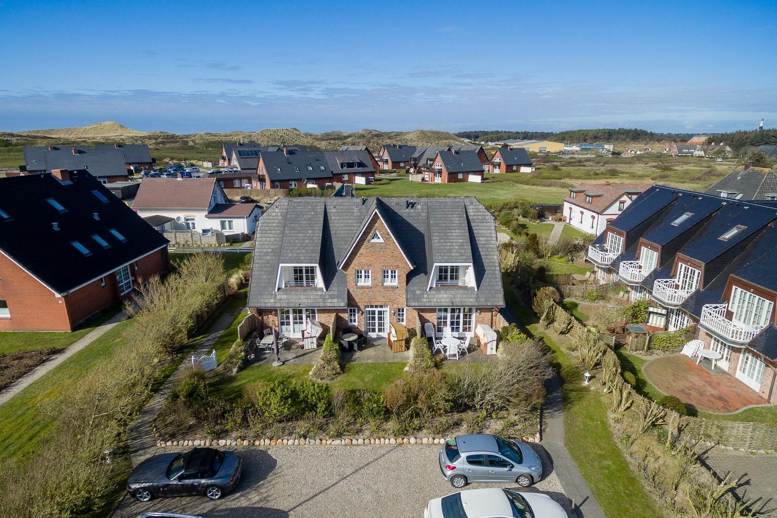 House with terrace and garden. Several cars parked in front of the house.