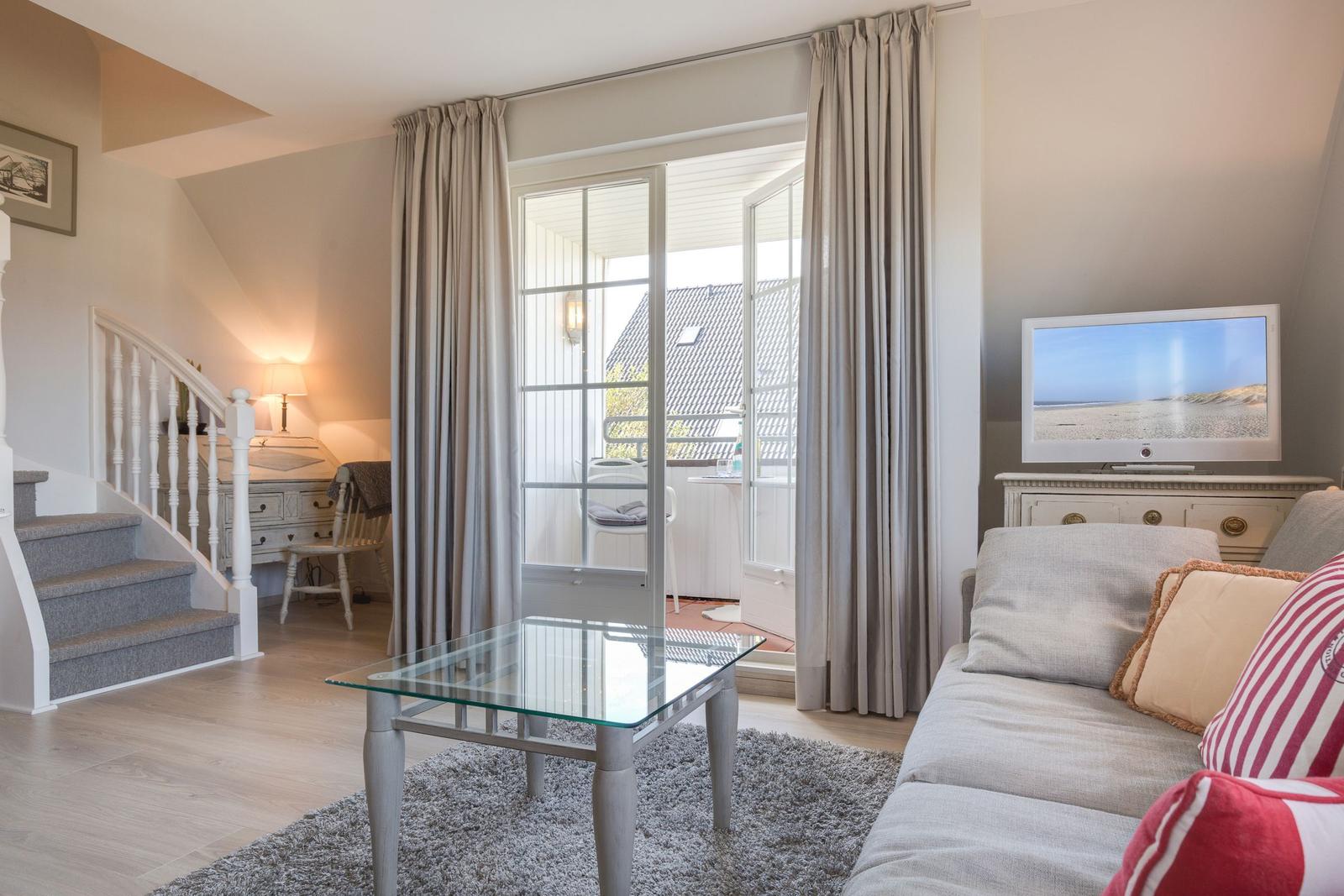 Living room with sofa, glass table, and balcony door. Staircase in the background.