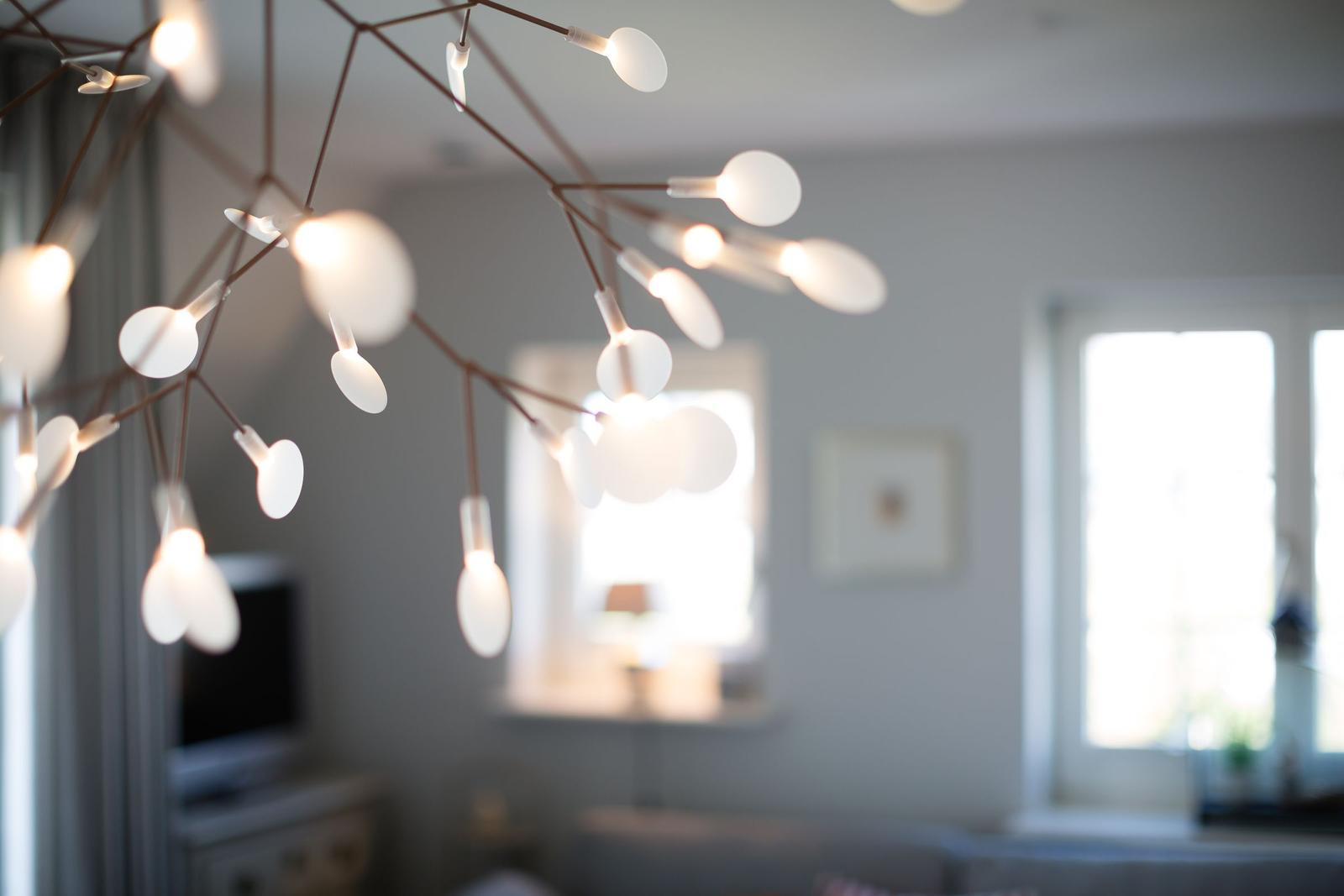 Modern ceiling light with many white lamps above a living area with windows.