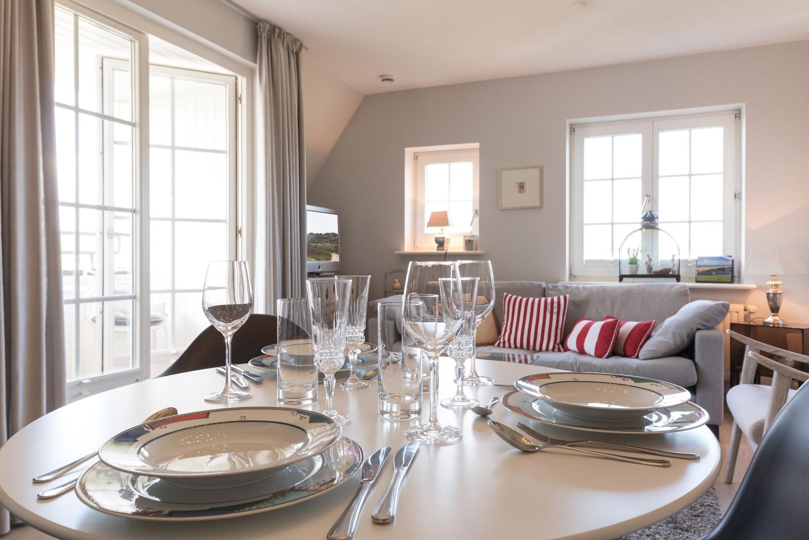 Set dining table with plates and glasses. Sofa with cushions in background.