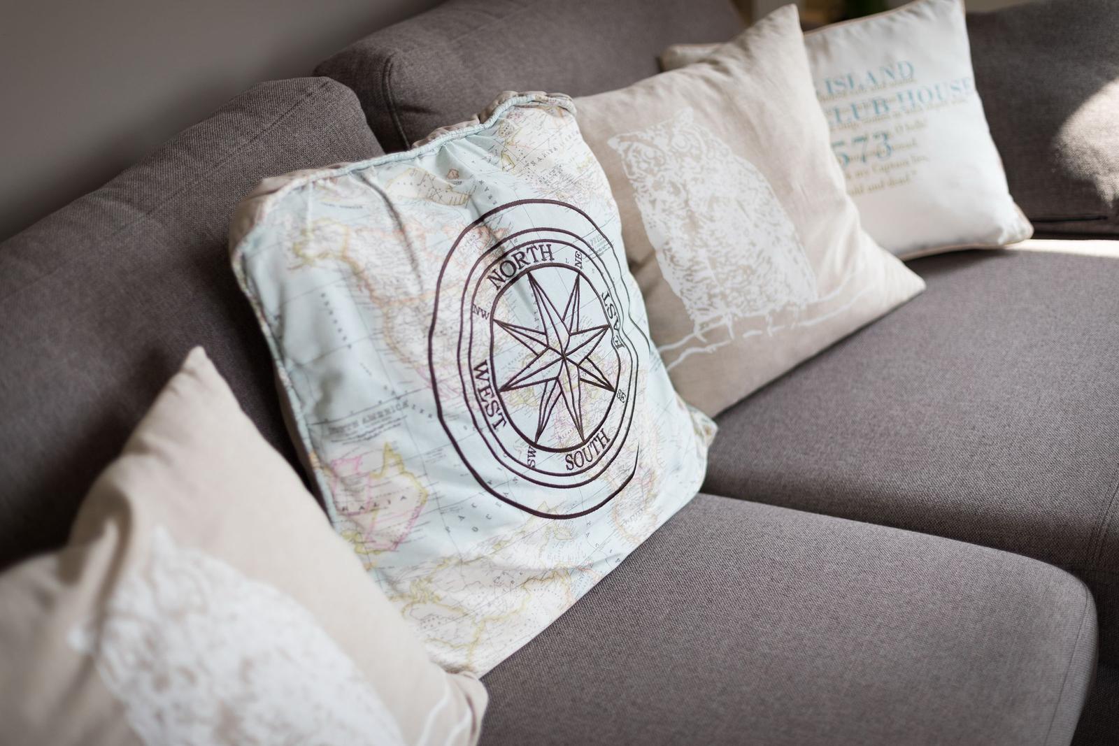 A gray sofa with cushions, one with compass pattern, others with text and ornaments.
