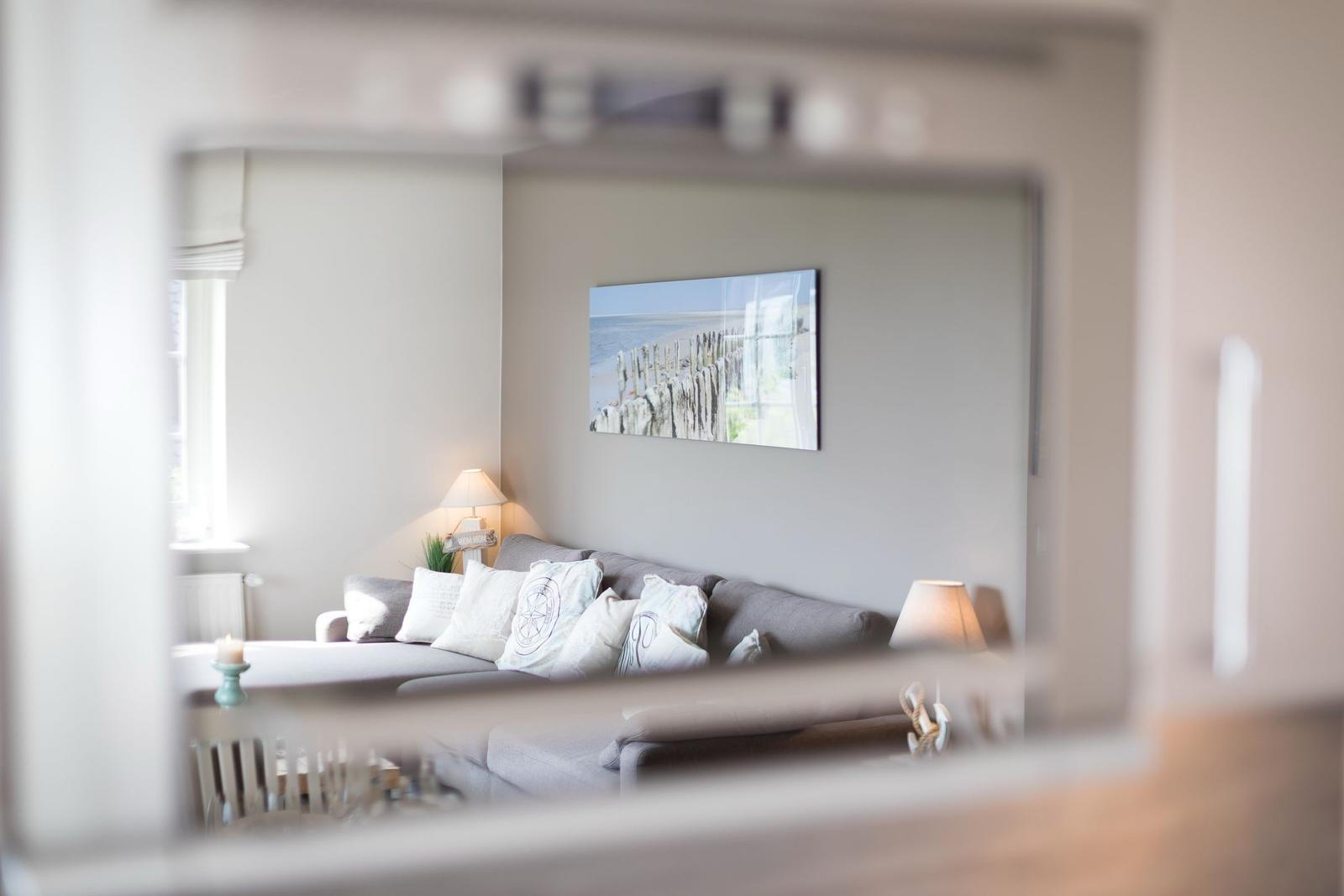 Living room with sofa, cushions, and wall art. View through a mirror frame.